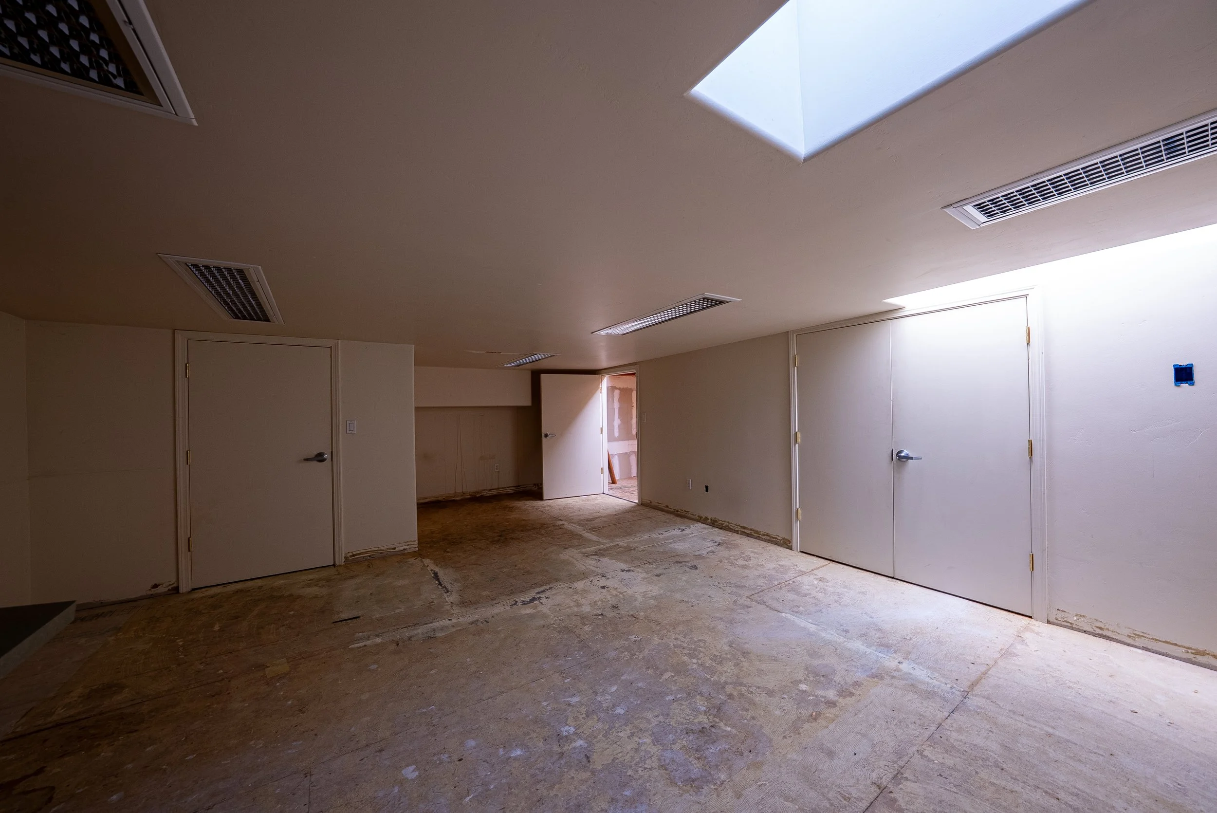 Empty room with new drywall and ceiling vents, some construction work visible.