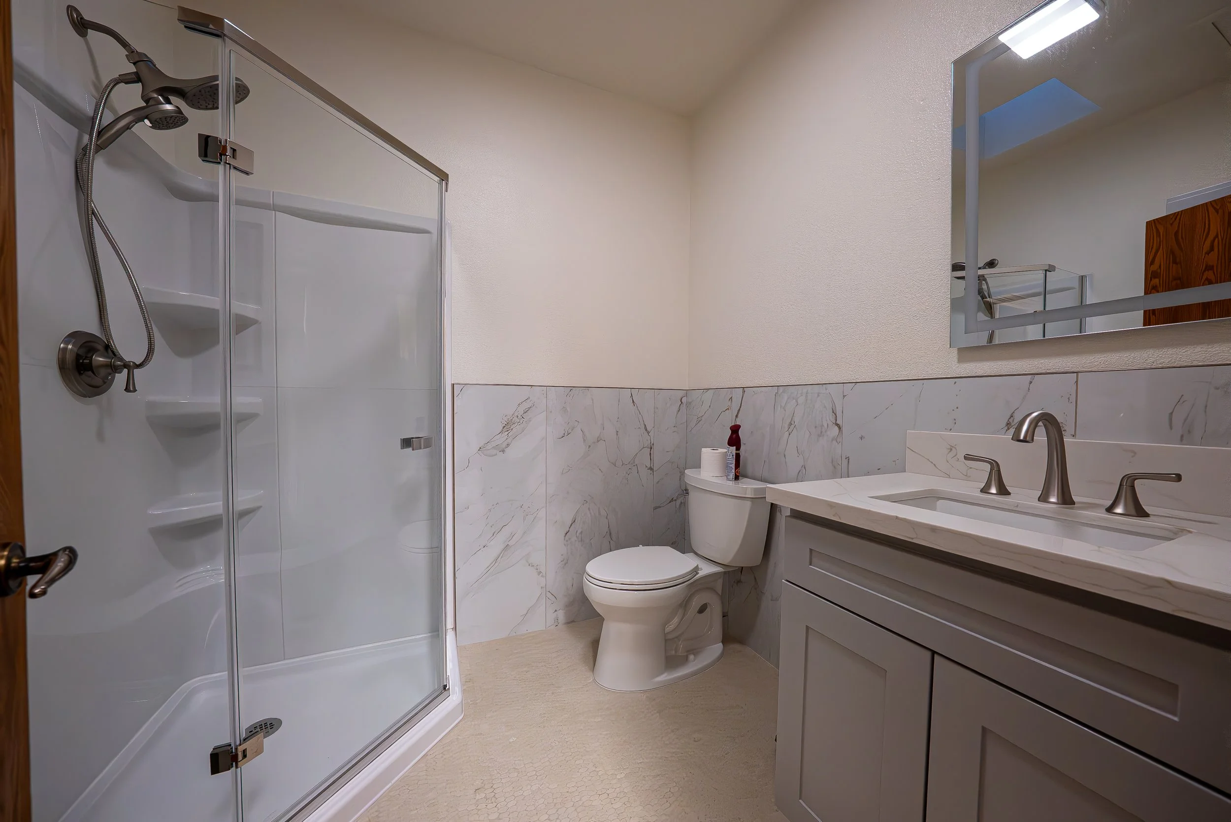 A modern bathroom with a shower enclosure, a toilet, a vanity with a sink, a mirror, and marble wall accents.