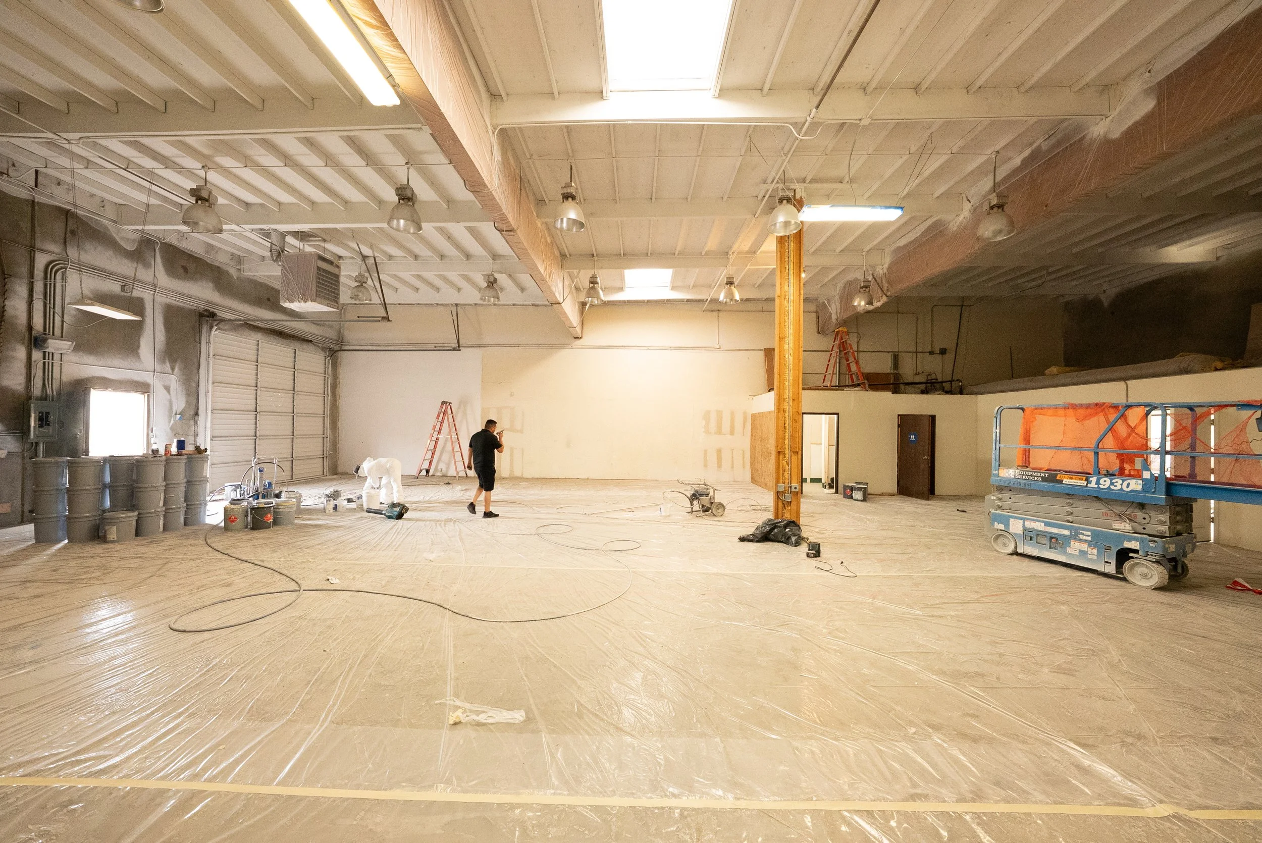 Interior of a large room under construction with workers, construction equipment, and unfinished walls.