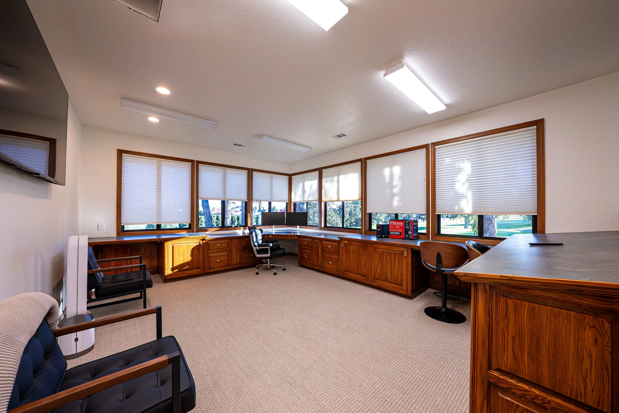 Office conference room with multiple windows, wooden furniture, black chairs, and ceiling lights.