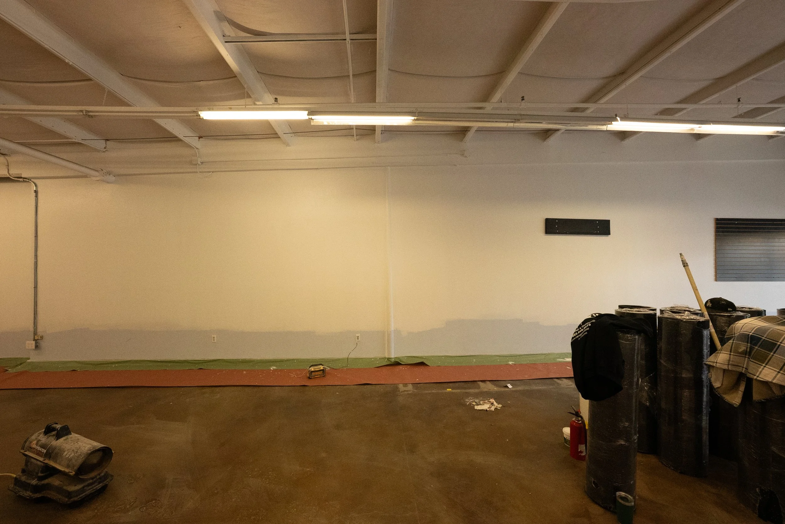 An unfinished interior room under construction with drywall, electrical wiring, and construction tools and materials scattered on the floor.