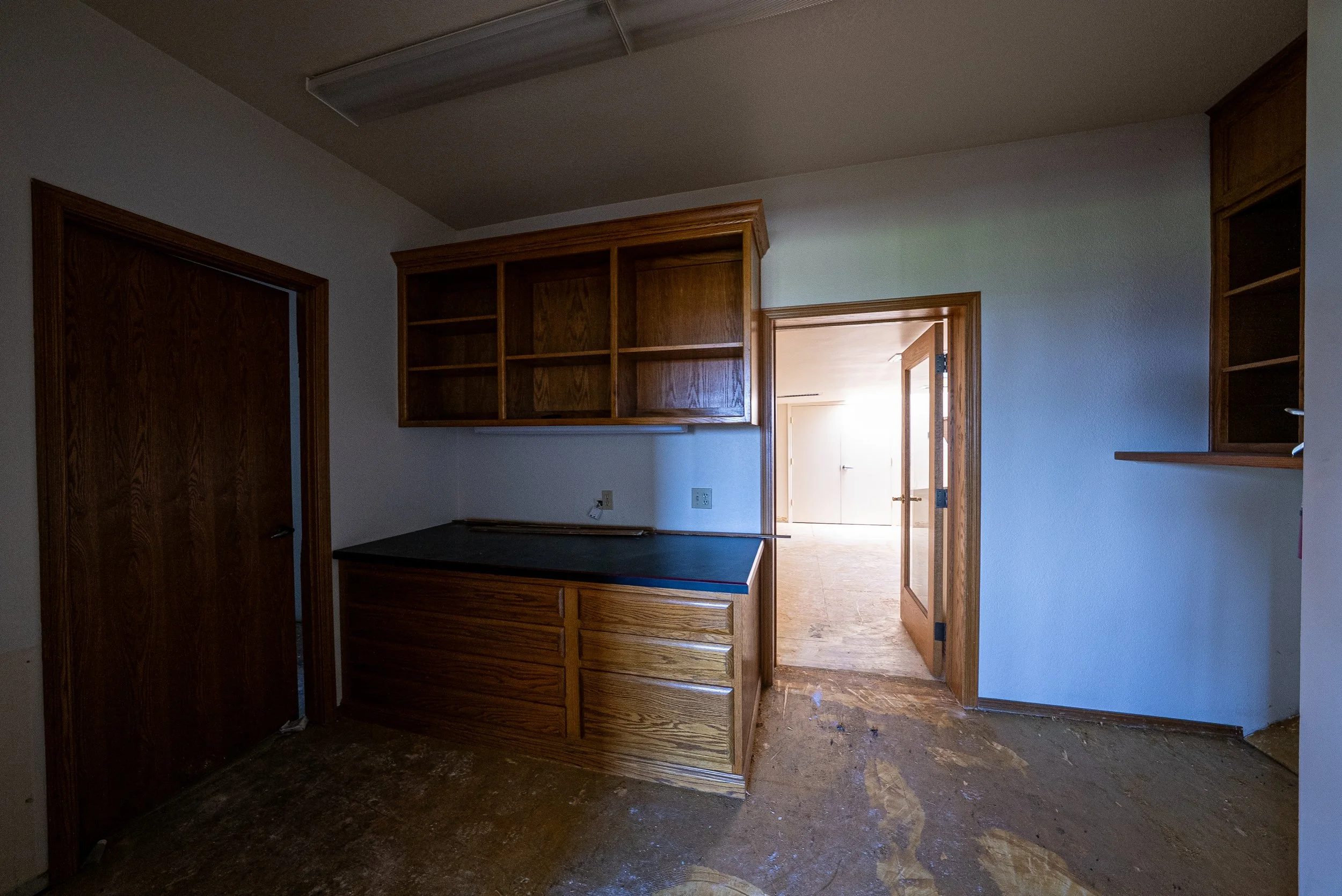 Interior of a room under renovation with wooden cabinets and door frames, a countertop, and construction debris on the floor.