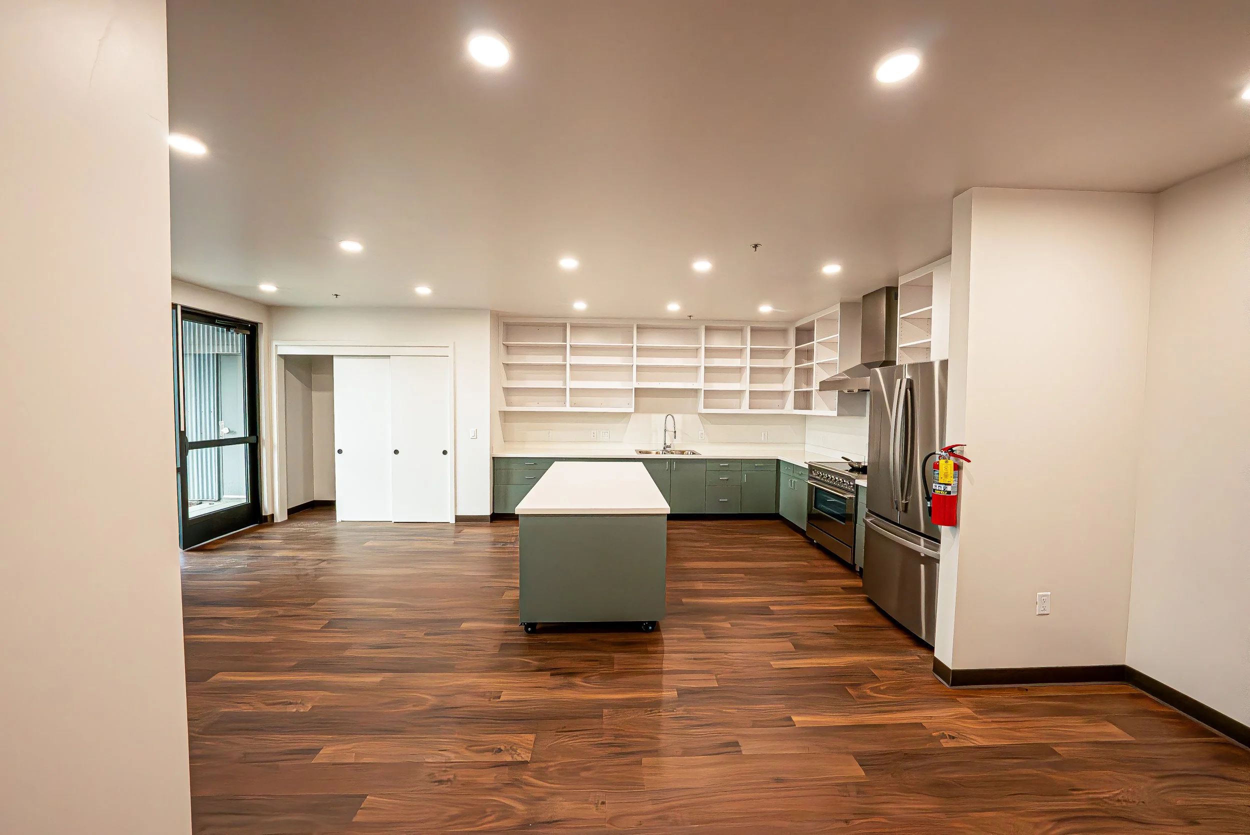 Modern kitchen with white upper cabinets, green lower cabinets, stainless steel appliances, a kitchen island, and dark wood flooring.