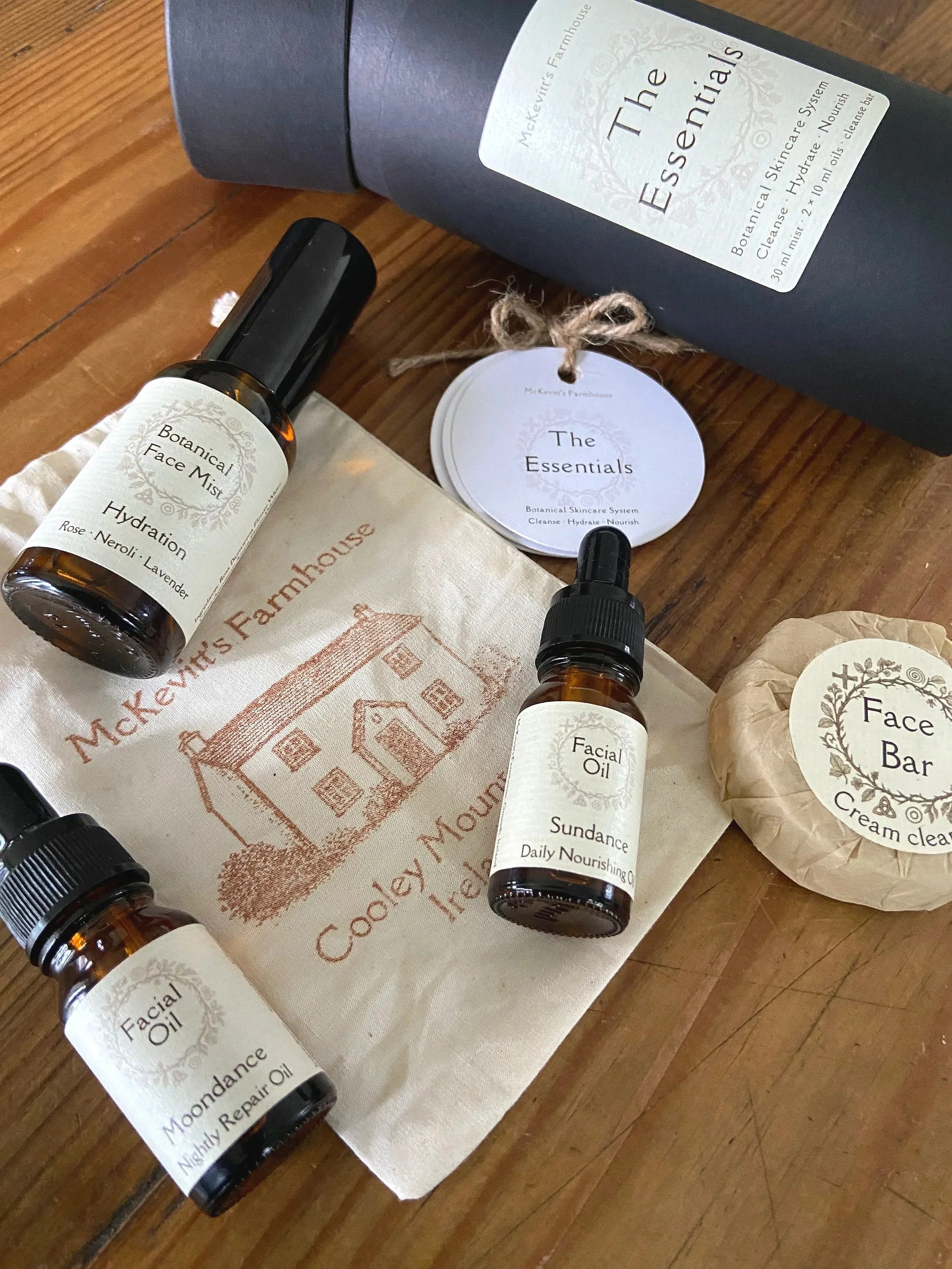 A collection of skincare products, including bottles of facial mist and facial oil, along with branded packaging and tags, displayed on a wooden surface.