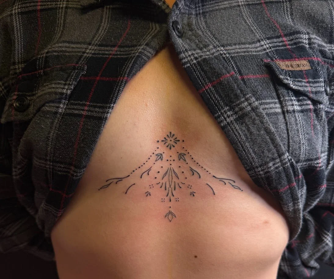 Tattoo of a simple, symmetrical floral and arrow design on person's lower ribcage.