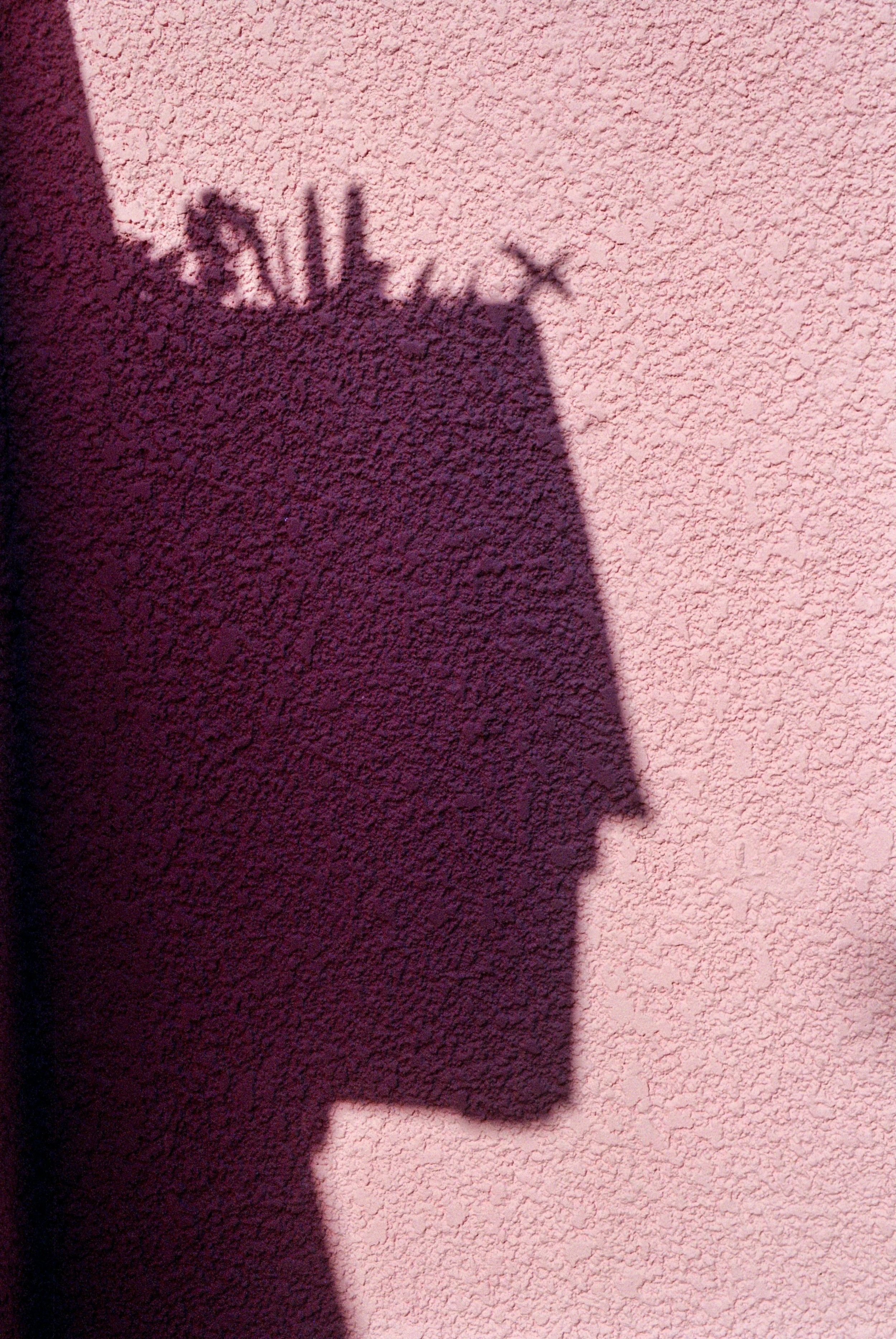 Shadow of a person's face on a pink textured wall