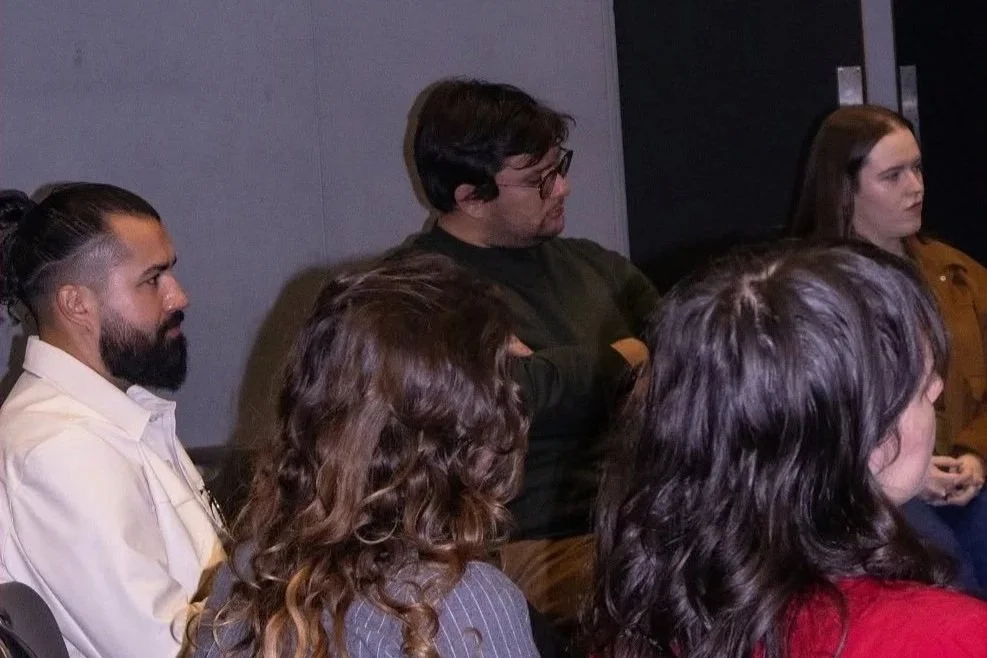 A group of people sitting and listening attentively at a meeting or conference in a dimly lit room.