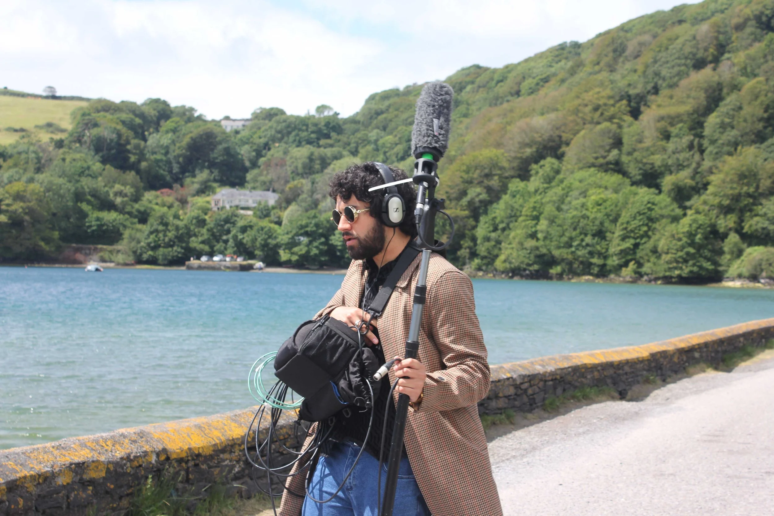 Jordan Murshed working as a location sound recordist, carrying a boom microphone and portable audio recording rig during a television production on location in Ireland.