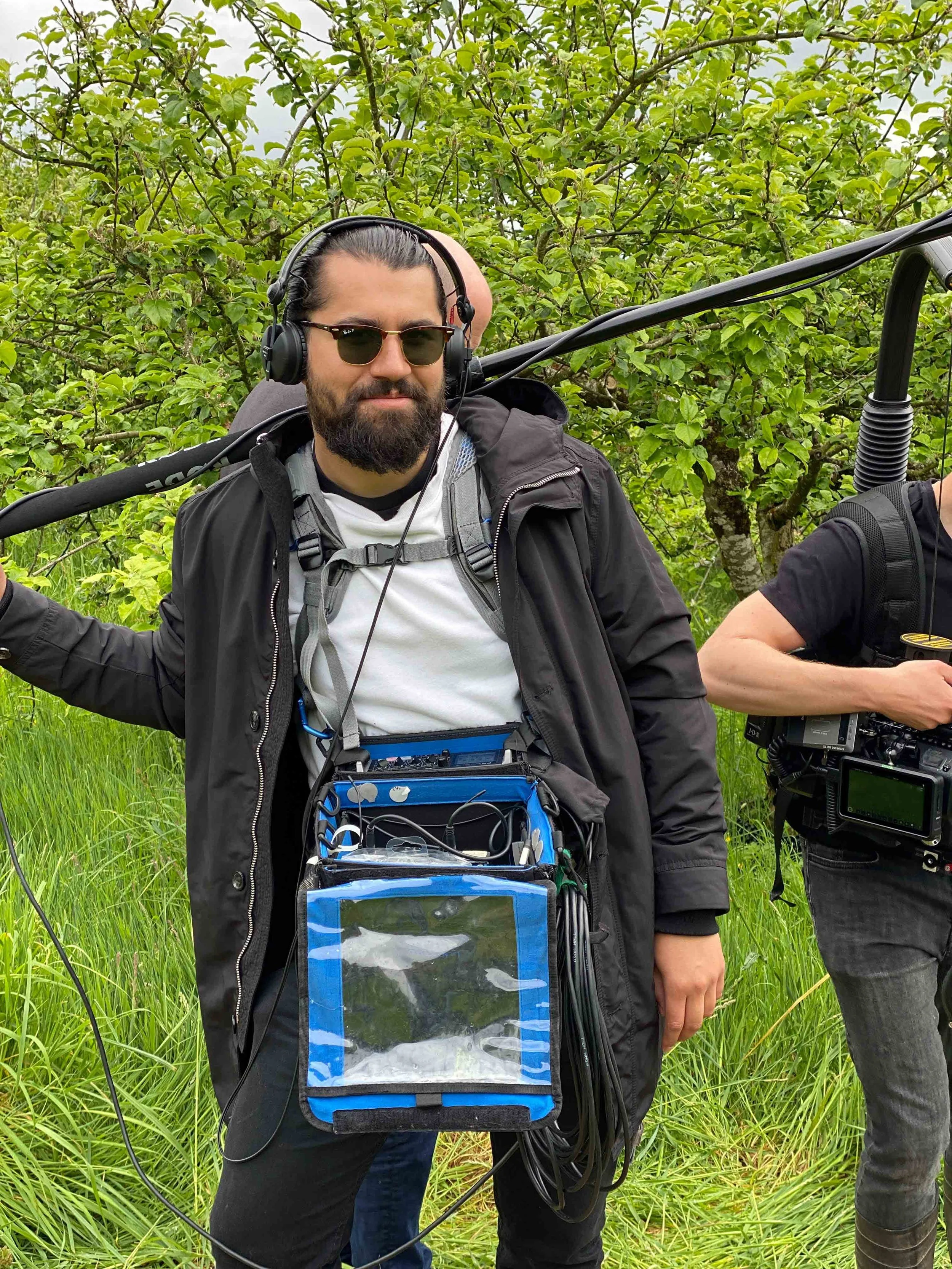 Jordan Murshed working as a location sound recordist with a bag based audio recording setup, headphones, and boom pole during a television production in Ireland.