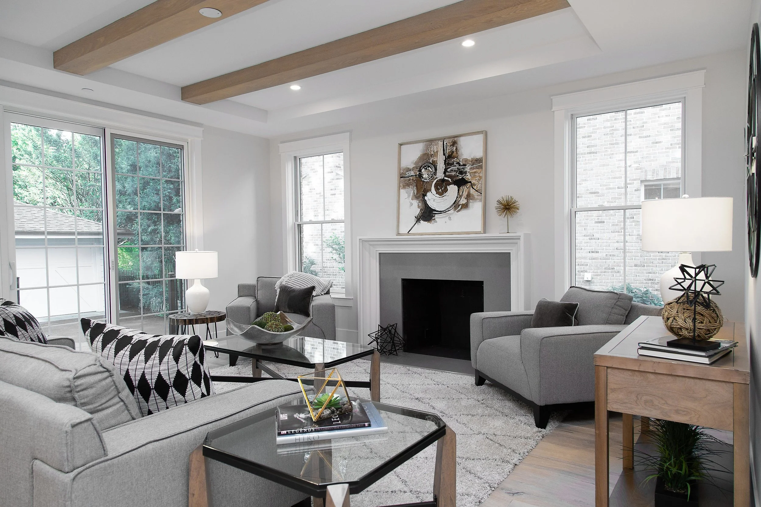 A modern living room with large windows, a fireplace, and contemporary decor including artwork, lamps, and decorative objects.