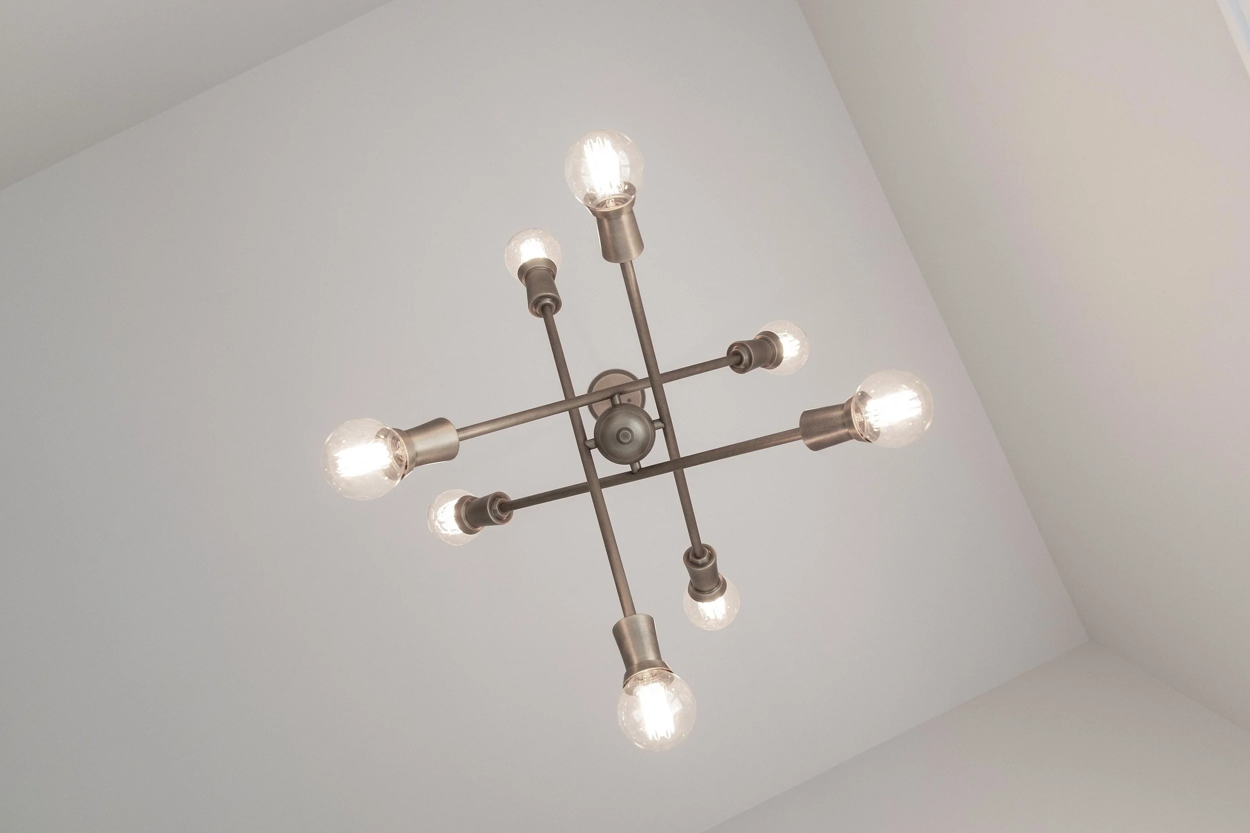 A modern chandelier with exposed bulbs hanging from a metallic fixture on a white ceiling.