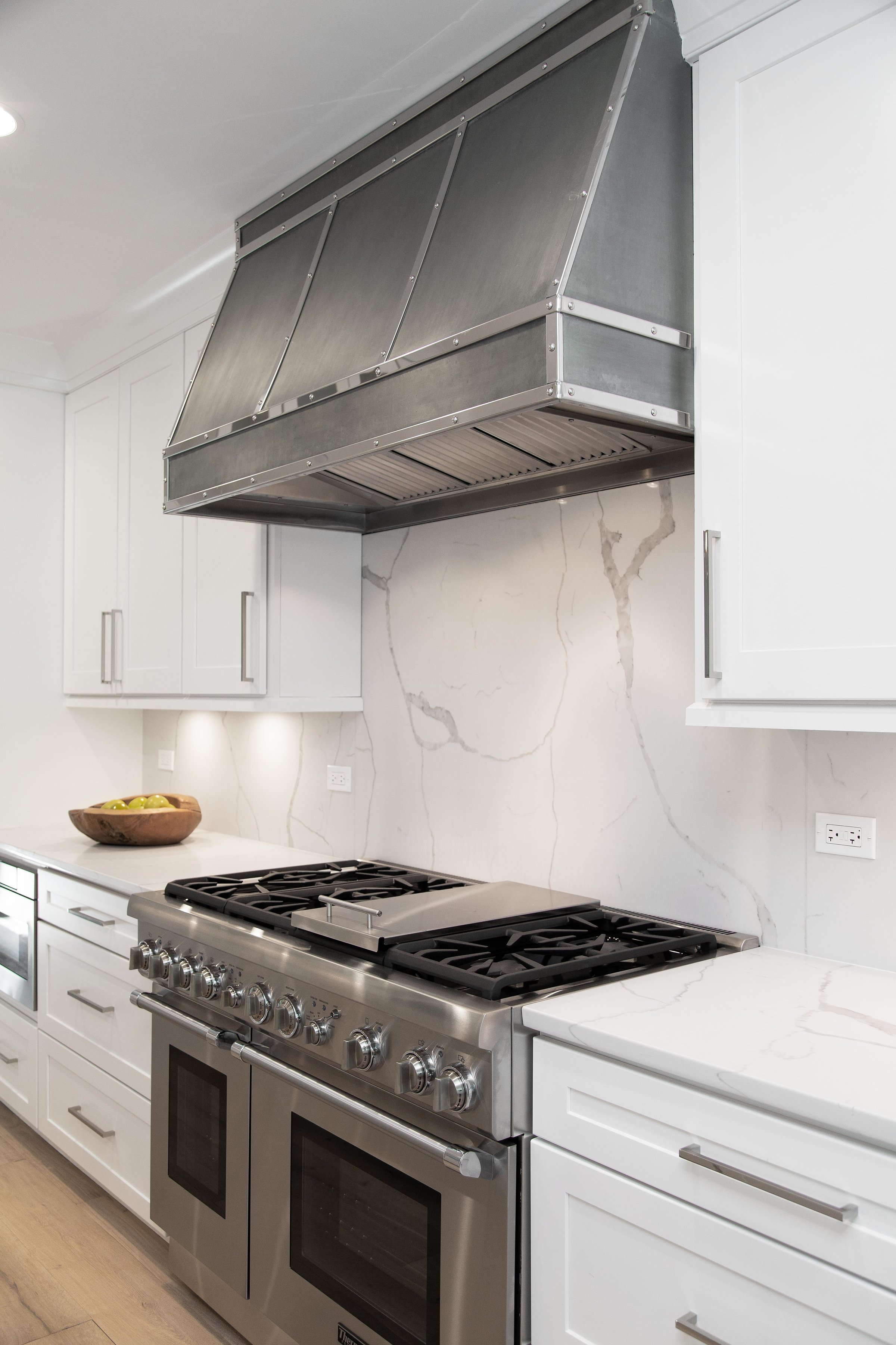 Modern kitchen with a stainless steel stove and oven, white cabinetry, a white marble backsplash, and a wooden bowl filled with apples on the counter.
