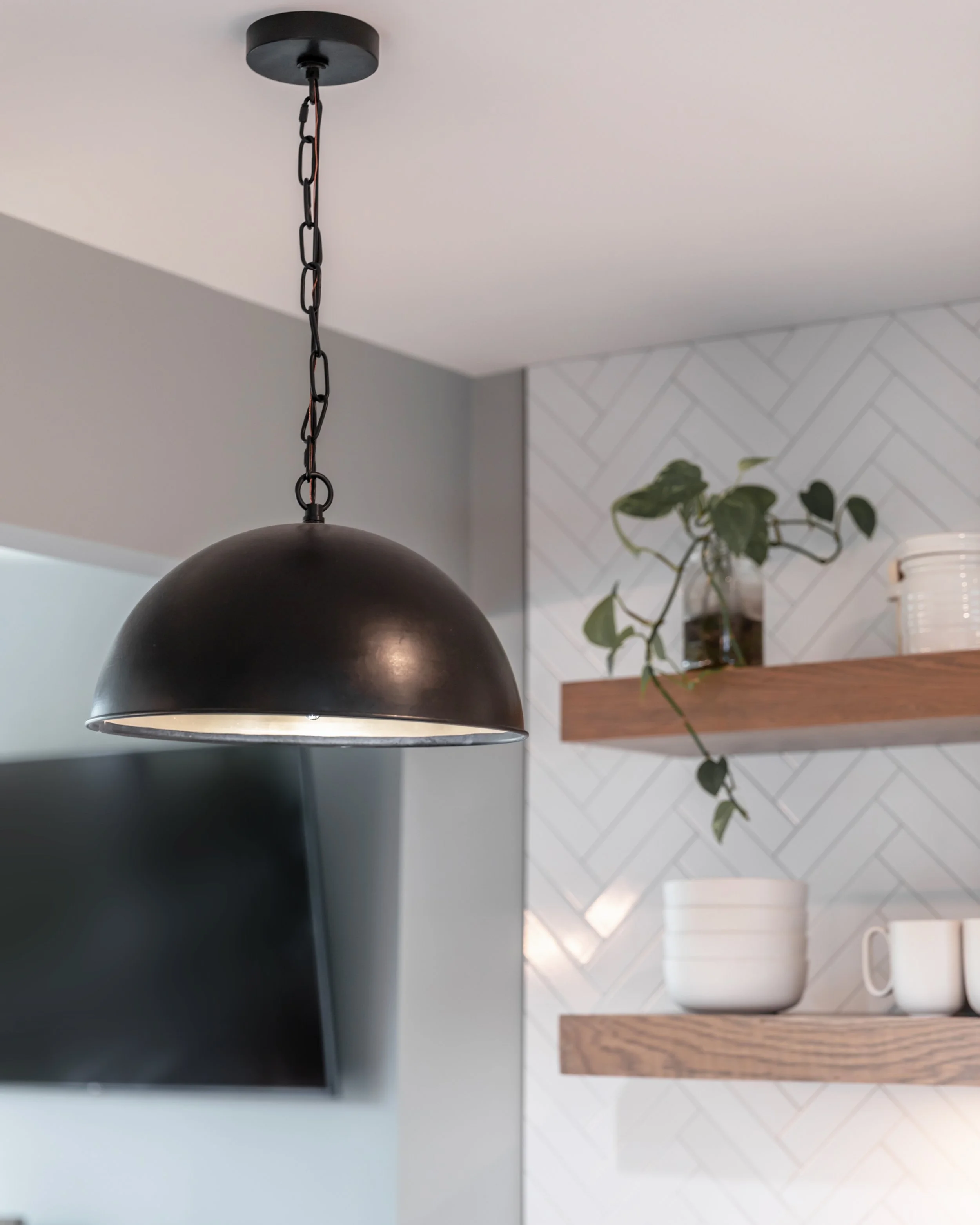 Close-up of a black pendant lamp with a black chain hanging from the ceiling in a modern room.