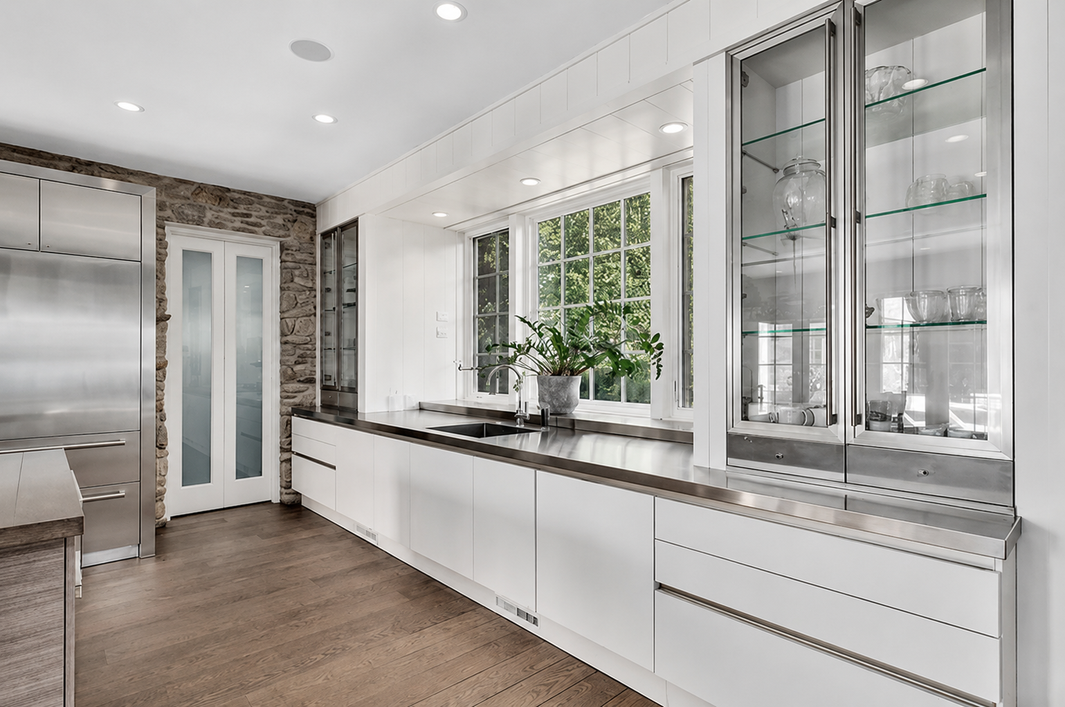 Modern kitchen with white cabinets, a stone wall, and large windows with a potted plant on the counter.