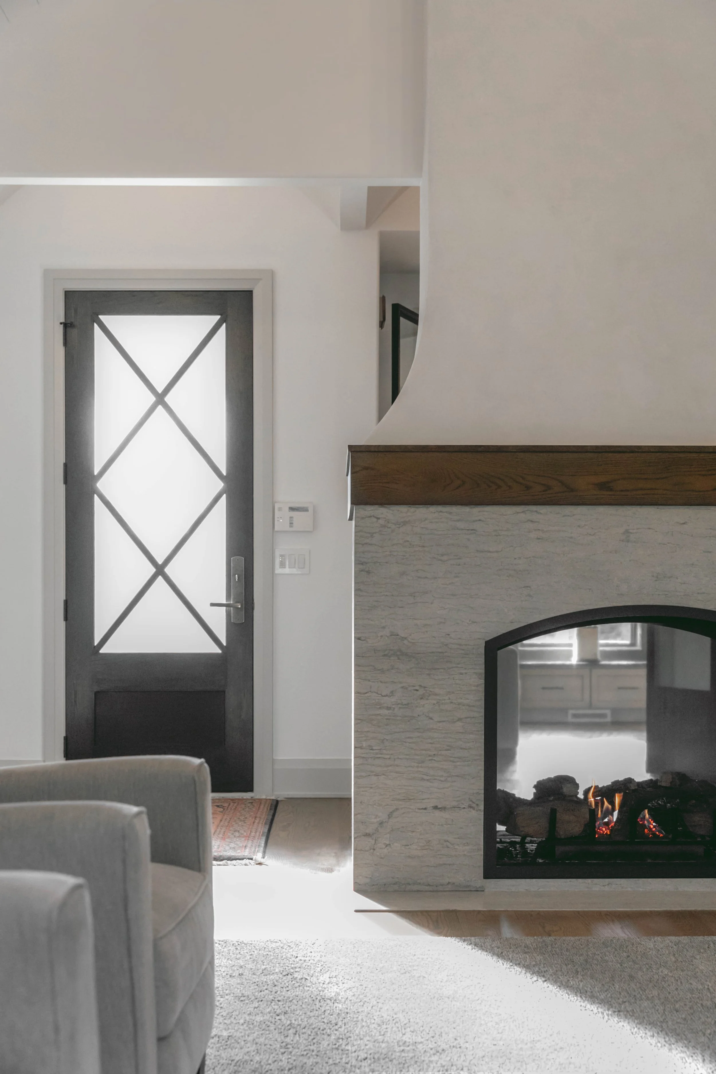Interior of a modern home with a gray door, a fireplace, a partial view of a white sofa, and a textured area rug.