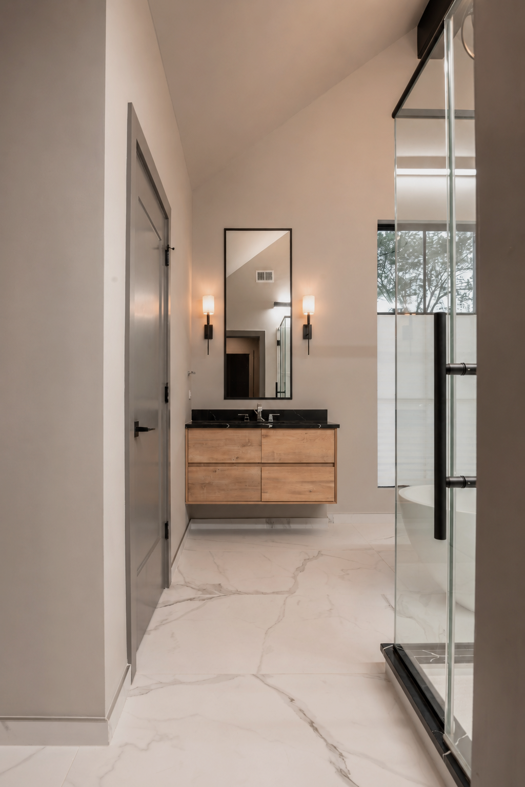 Modern bathroom with a wooden vanity, black countertop, large mirror, wall sconces, marble floor, and a glass shower enclosure.