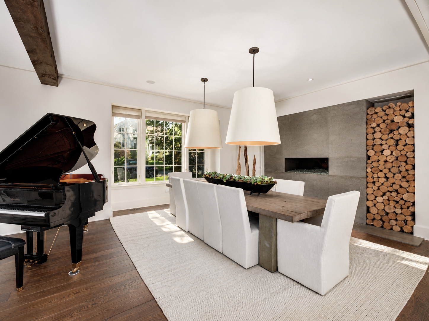 Living room with a grand black piano, a large window, a wooden dining table with white chairs, a modern fireplace, and a built-in wood storage.