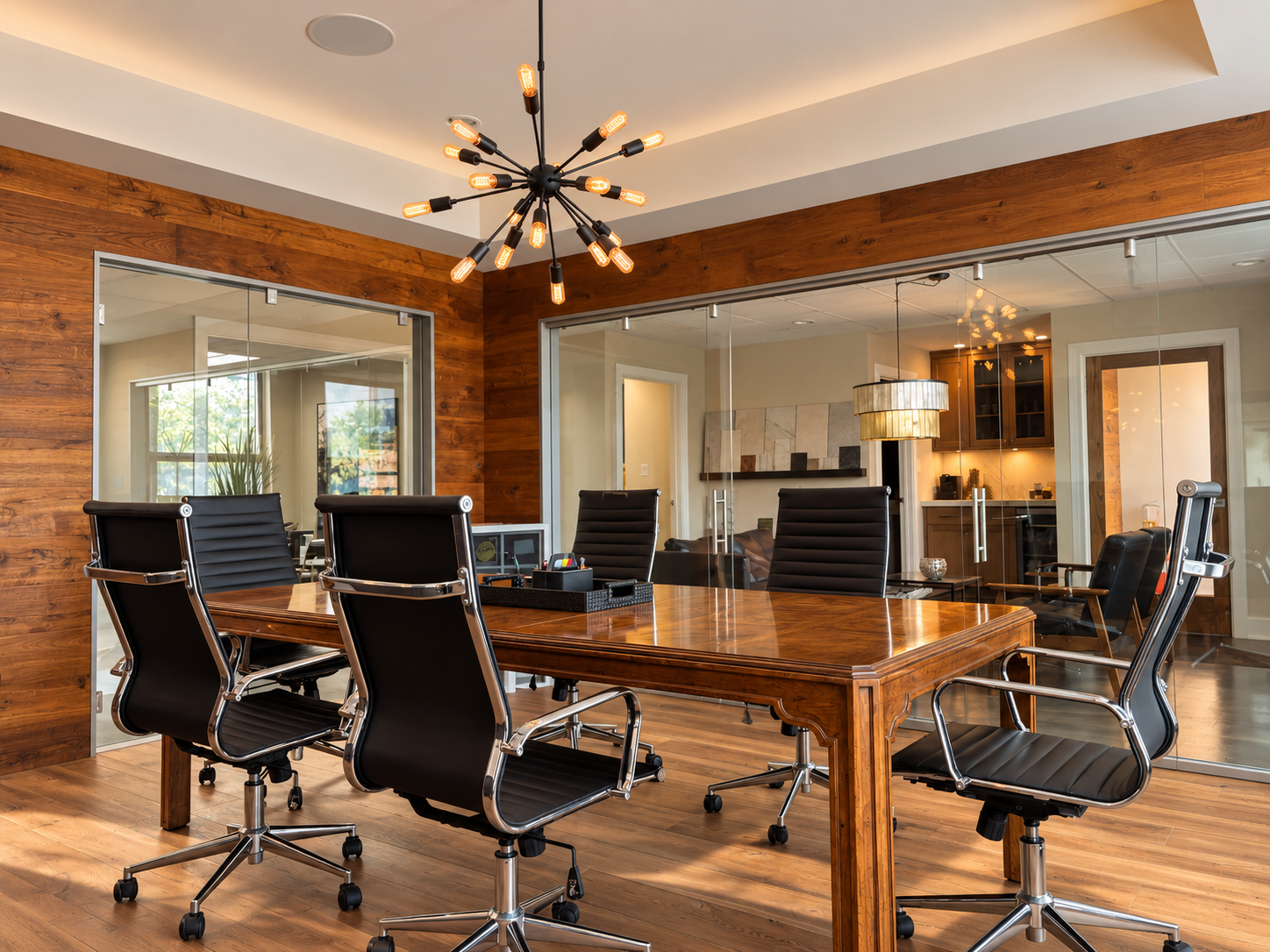 Modern conference room with wooden table, black leather office chairs, glass walls, and contemporary lighting fixtures.