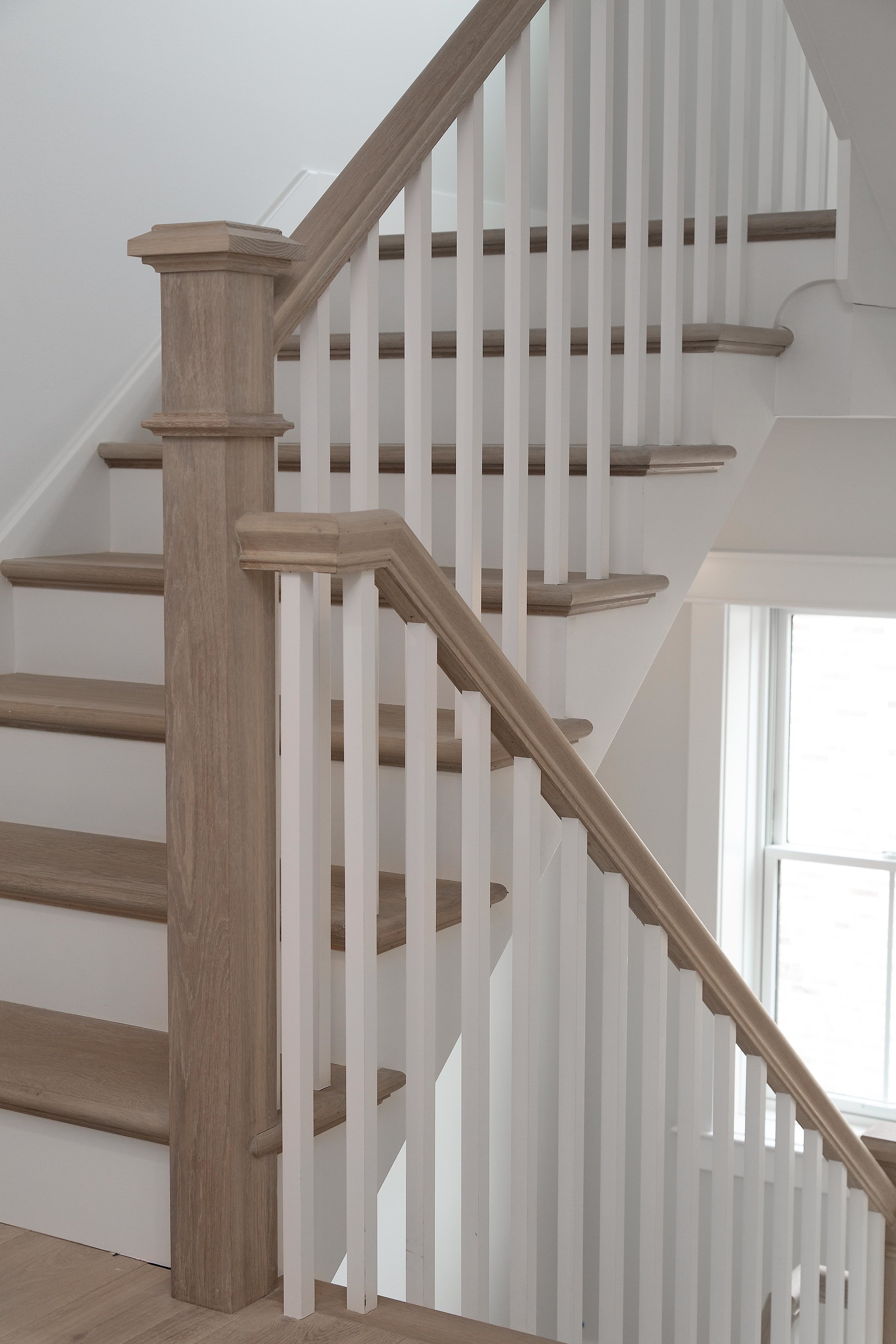 Interior view of a staircase with wooden handrail and white balusters, near a window.