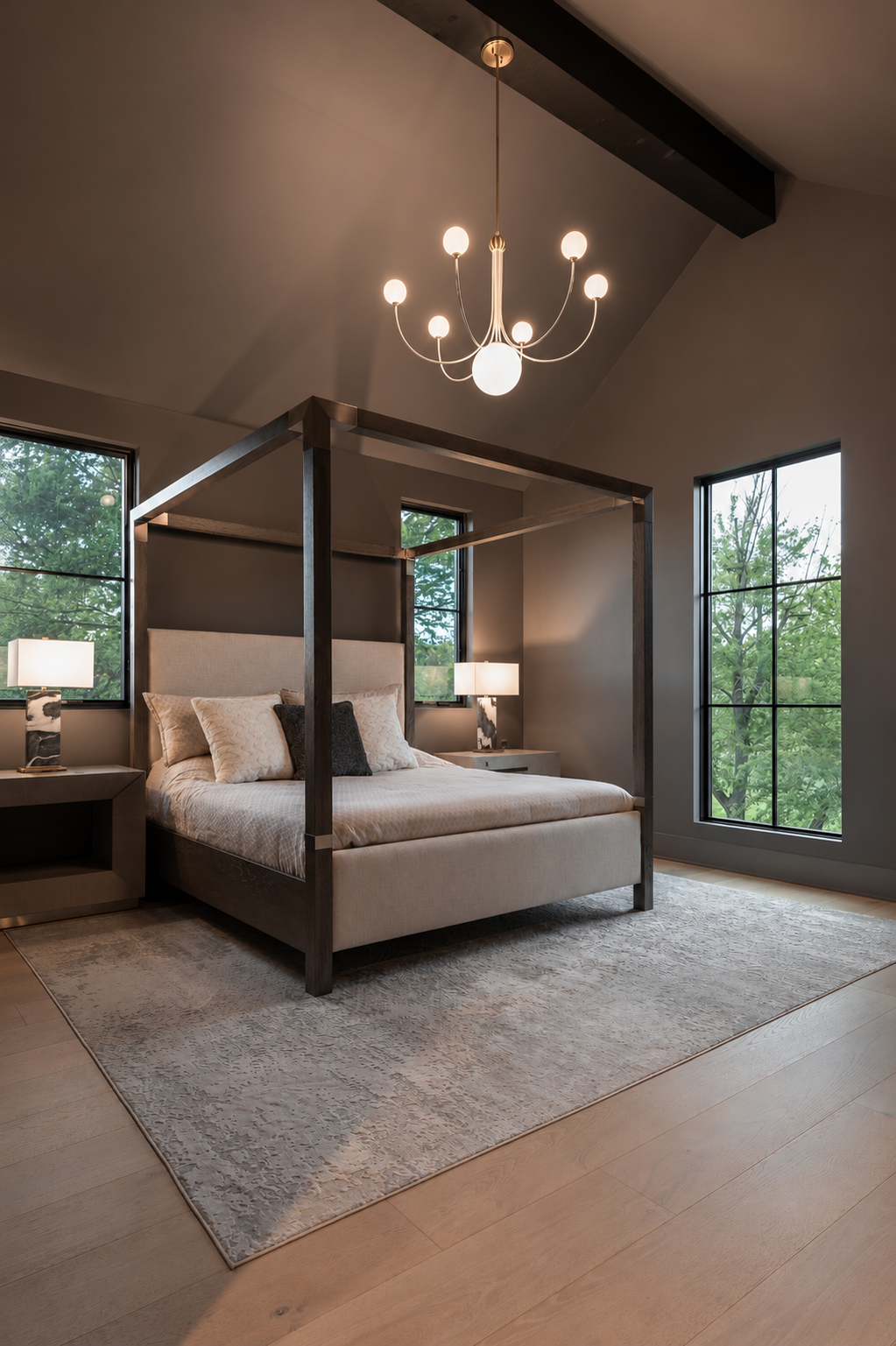Contemporary bedroom with a four-poster bed, beige bedding, and dark wood accents, illuminated by modern pendant and table lamps, and surrounded by large windows showing greenery outside.
