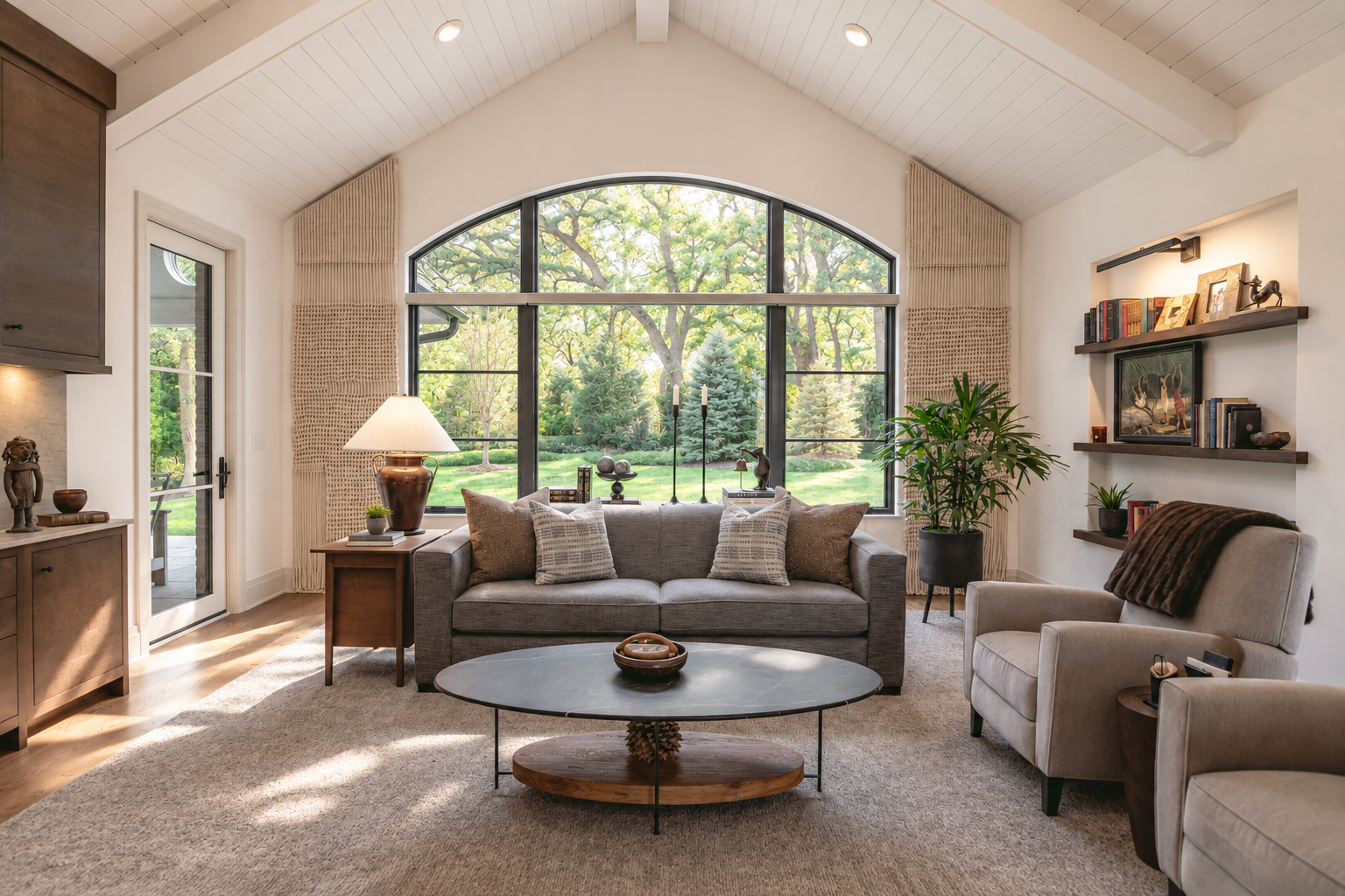 Living room with large arched window overlooking a green garden, featuring a sofa, armchair, coffee table, and decorative shelves.