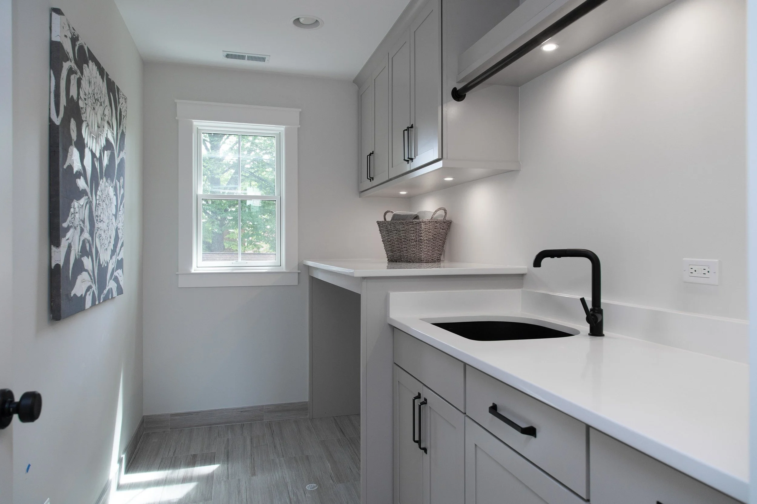 Small modern kitchen with white cabinets, a black sink, and a window overlooking green trees, decorated with a black and white pattern on the wall.