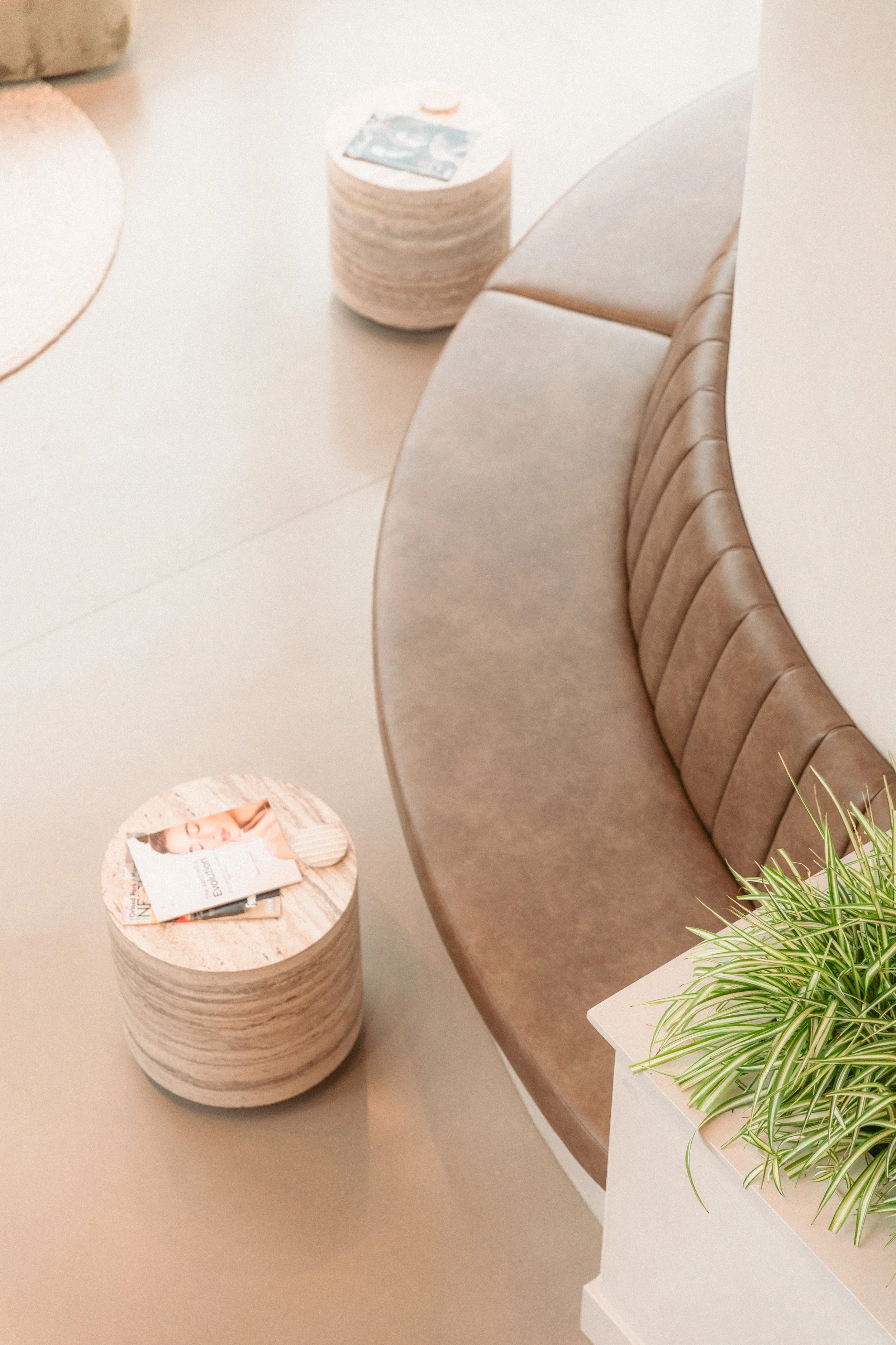 Round wooden side tables with magazines and a small plant on a white shelf beside a beige cushioned bench.