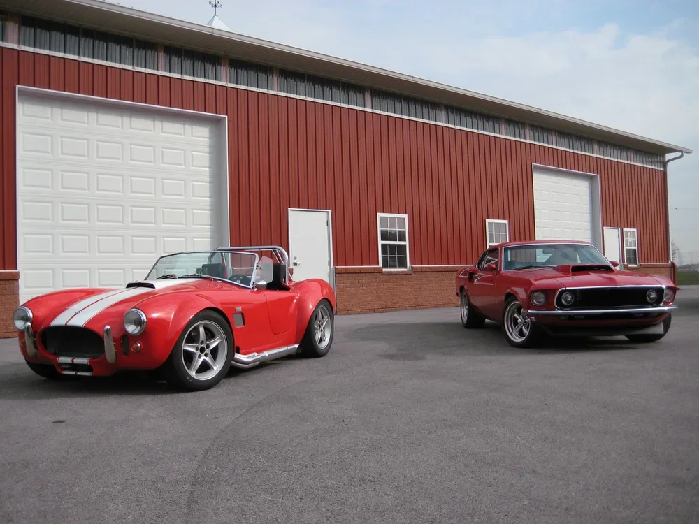 Two red classic cars parked outside a red and white building with garage doors.