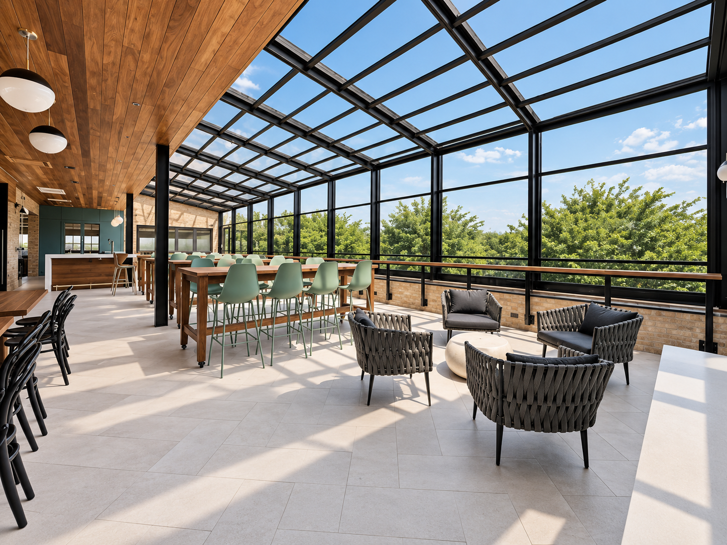 Bright indoor space with a glass ceiling and large windows overlooking trees, featuring modern seating including black woven chairs and mint green barstools around a wooden counter, with a wooden ceiling and pendant lights.