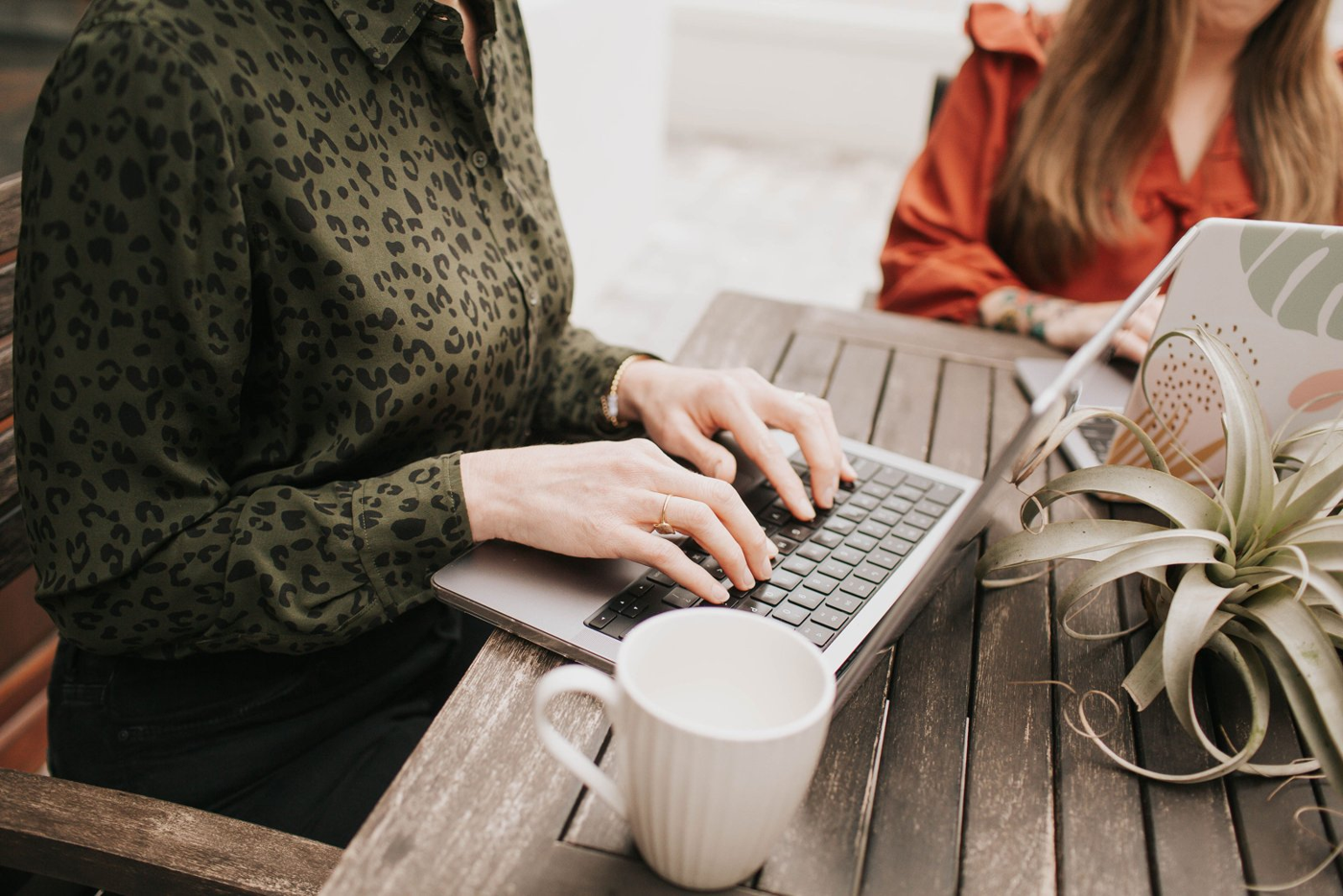 A team member typing on a laptop at an outdoor table while Natalie Clarke works alongside