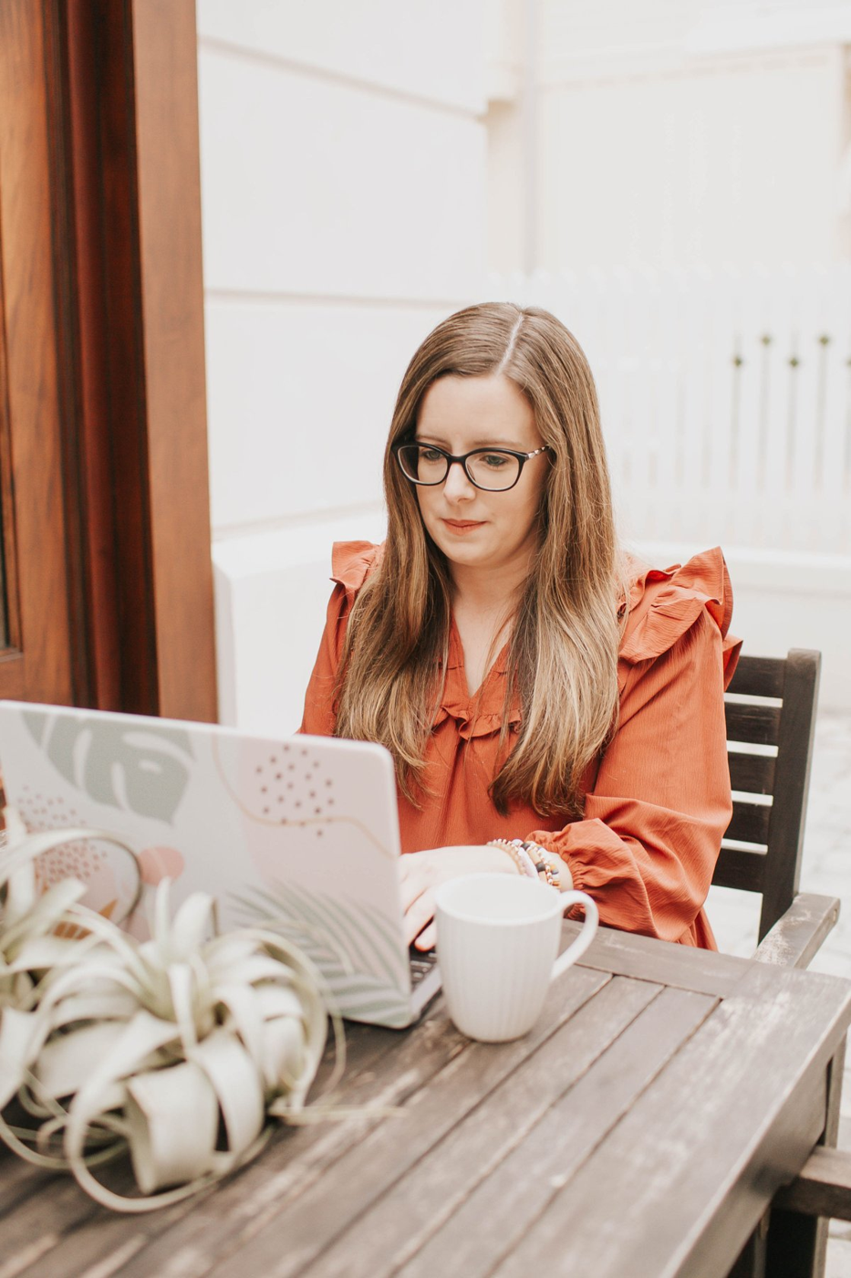 Natalie Clarke smiling at her laptop at an outdoor café table