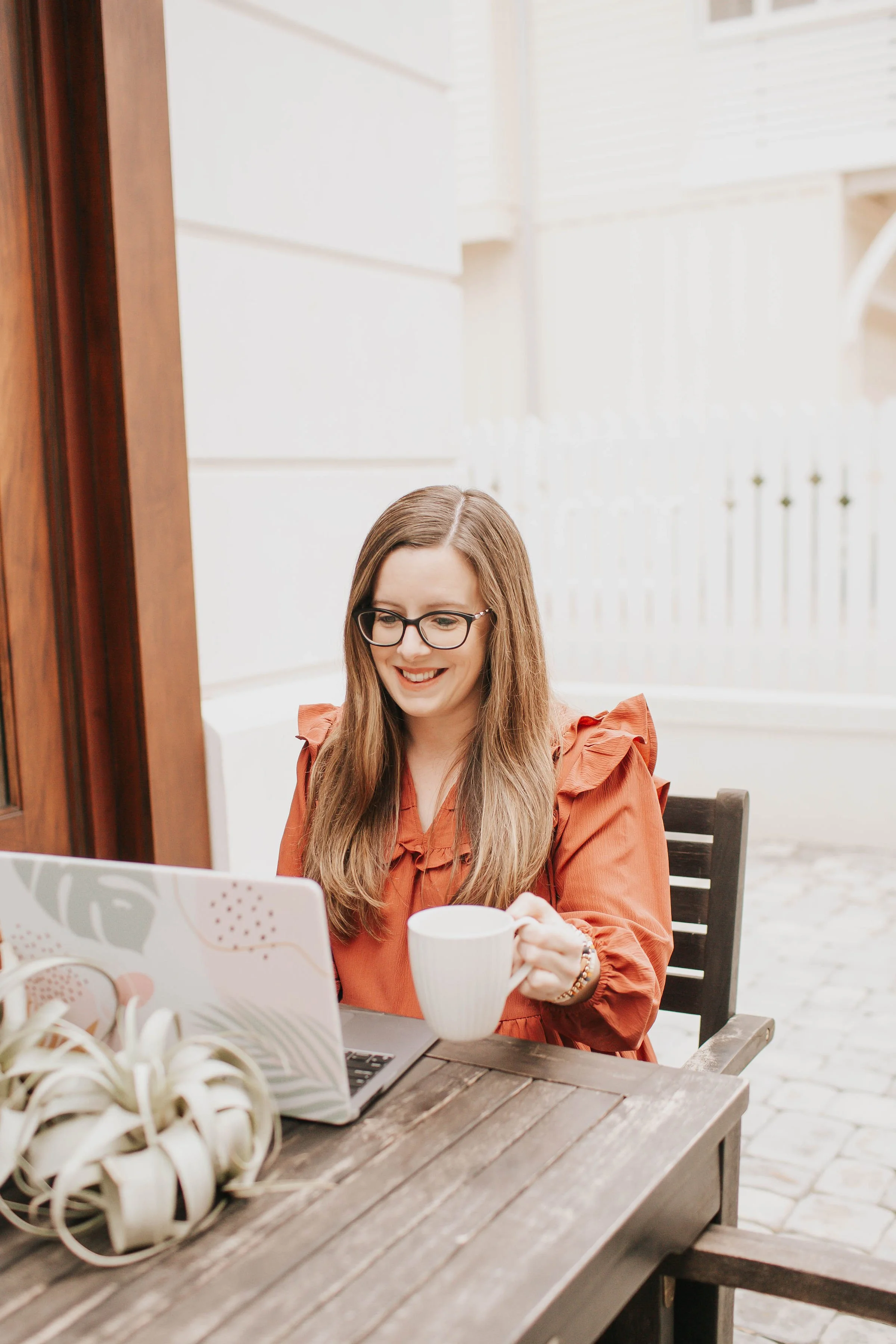 Natalie Clarke smiling while working on her laptop at an outdoor cafe table