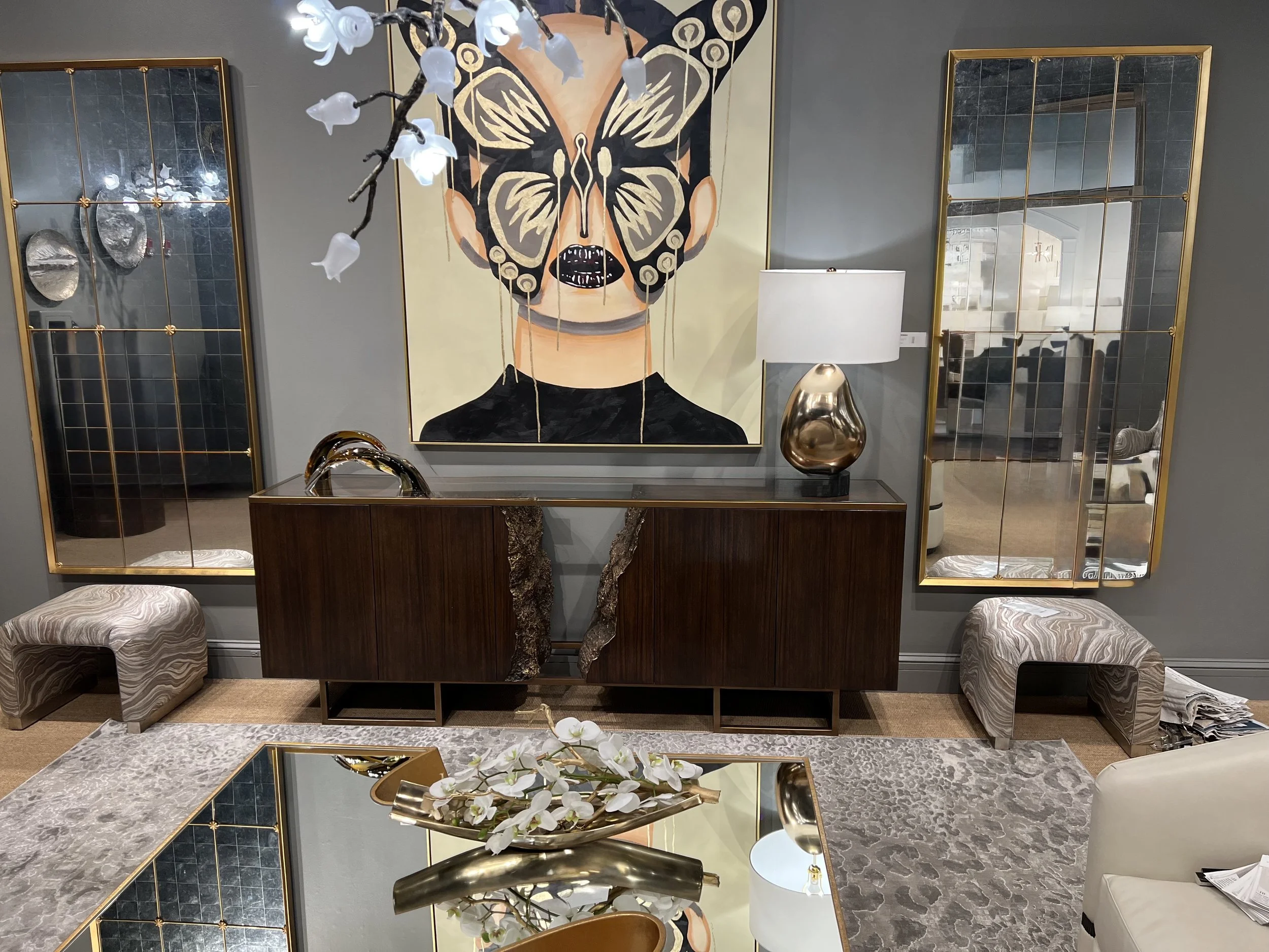 Interior decor with a large butterfly portrait, gold-framed mirrors, a table with a marble top, decorative items, tissues, and floral arrangements.