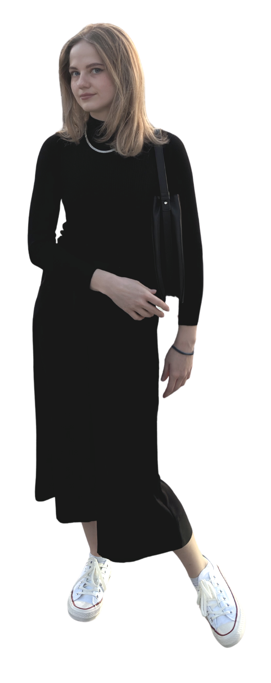 A young woman with light brown hair dressed in a black long-sleeve dress and white sneakers, carrying a black handbag, standing outdoors.