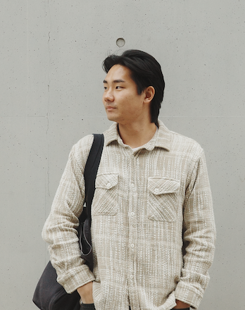Young man standing against a gray concrete wall with a black shoulder bag