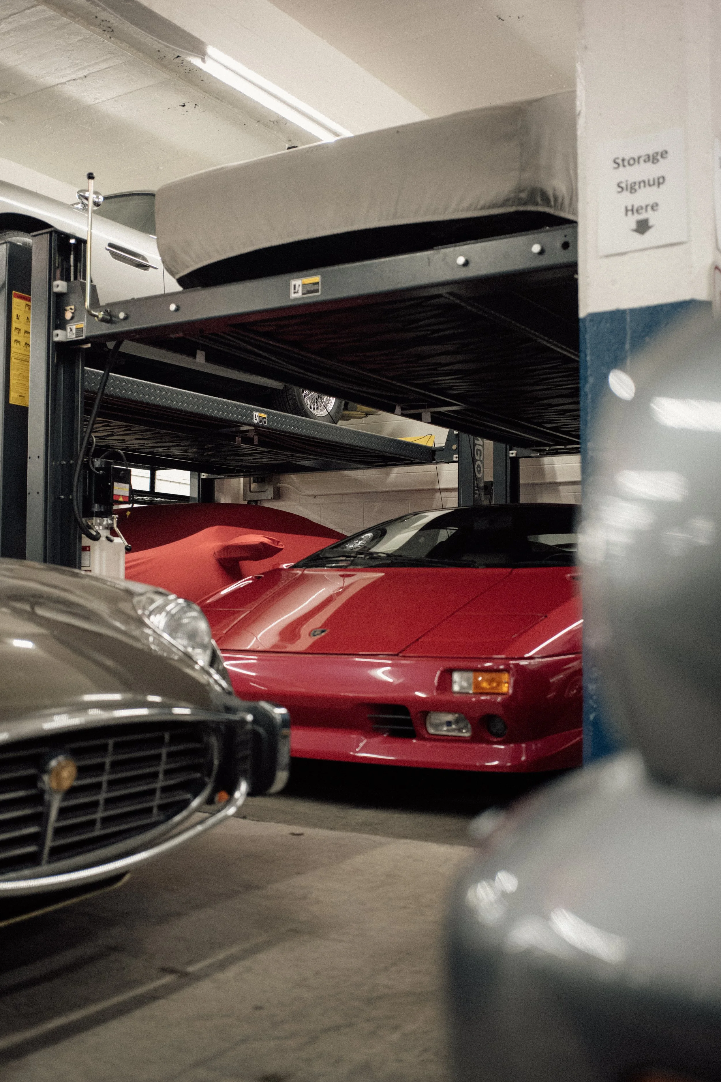Multiple cars parked in a parking garage, view from between two parked vehicles, some are visible on upper and lower levels.
