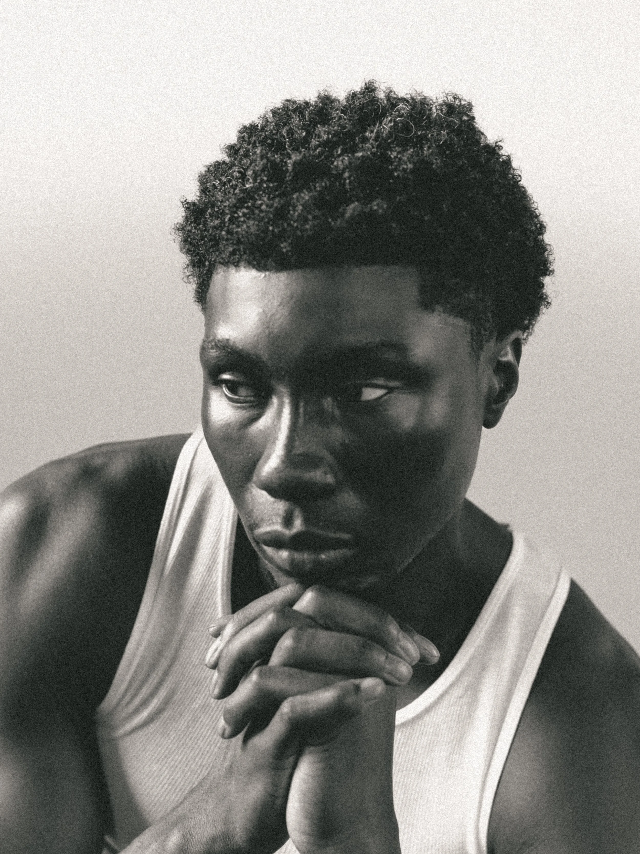 A young person with short curly hair, wearing a sleeveless shirt, looking down and touching their chin with their fingers. Columbus, Ohio, David Kim Photography