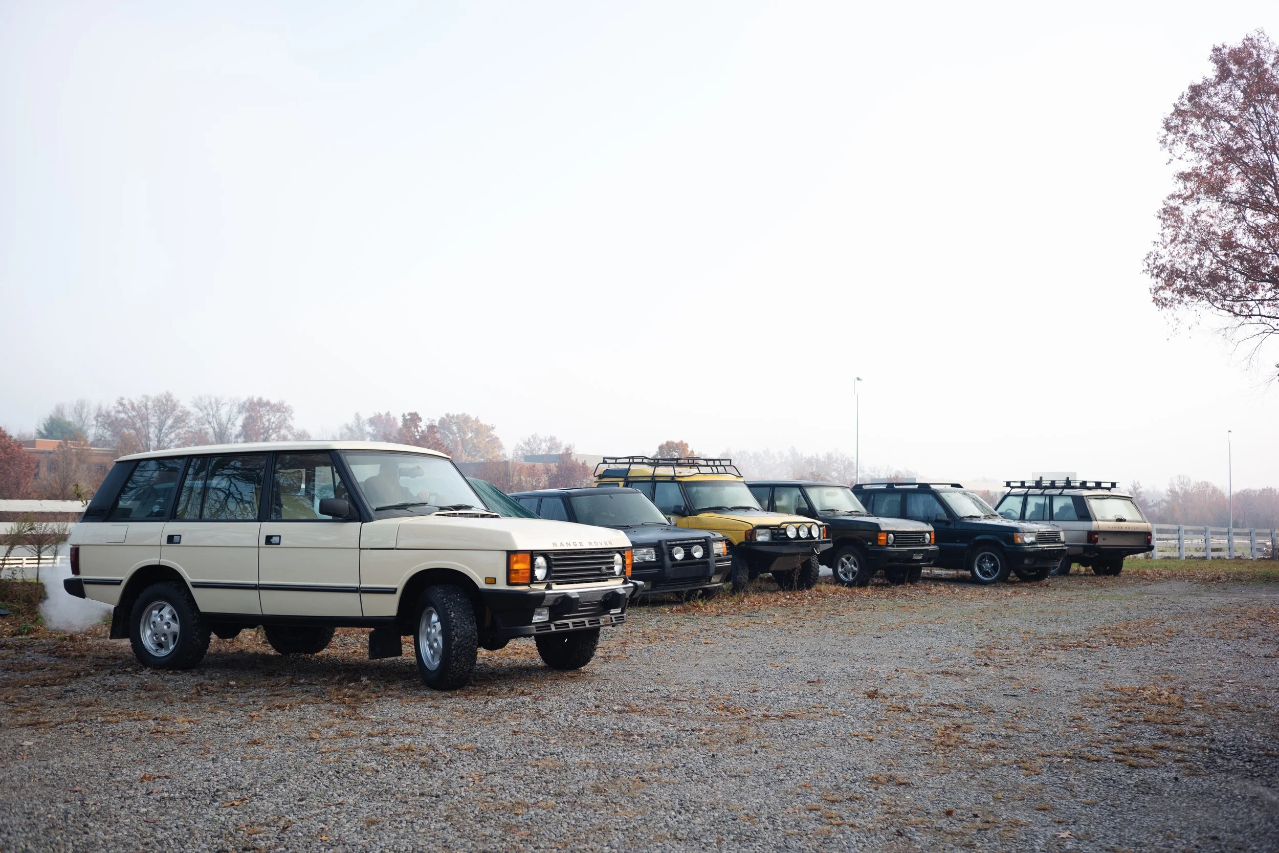 A row of vintage SUVs parked on a gravel lot, with trees and a clear sky in the background. Columbus, Ohio, David Kim Photography