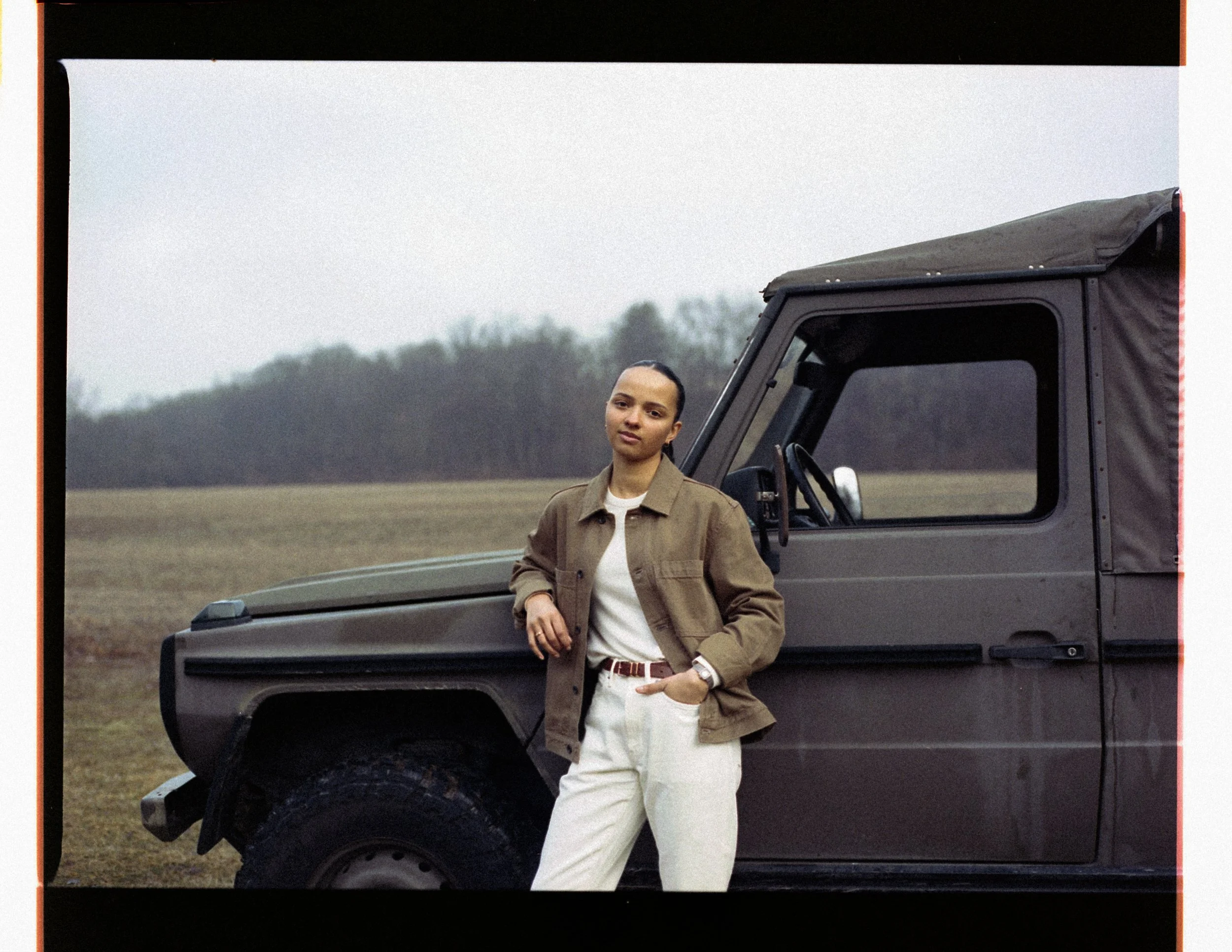 Young woman standing next to a black off-road vehicle outdoors in a field with trees in the background. Columbus, Ohio, David Kim Photography