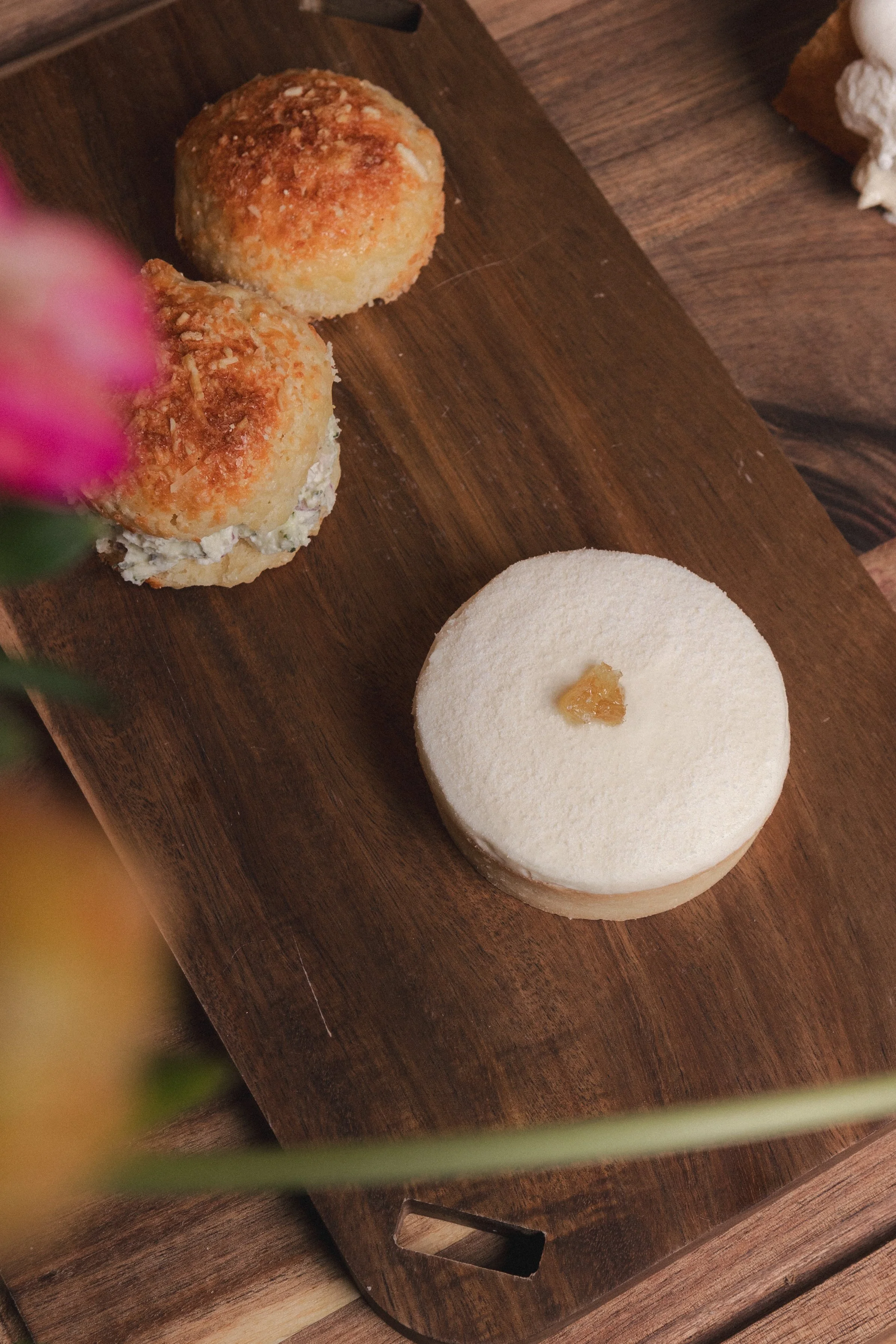 Close-up of two round fried appetizers or desserts with a breadcrumb topping on a wooden serving board. Part of a white, round dessert with a small dollop of some topping is also visible. Columbus, Ohio, David Kim Photography