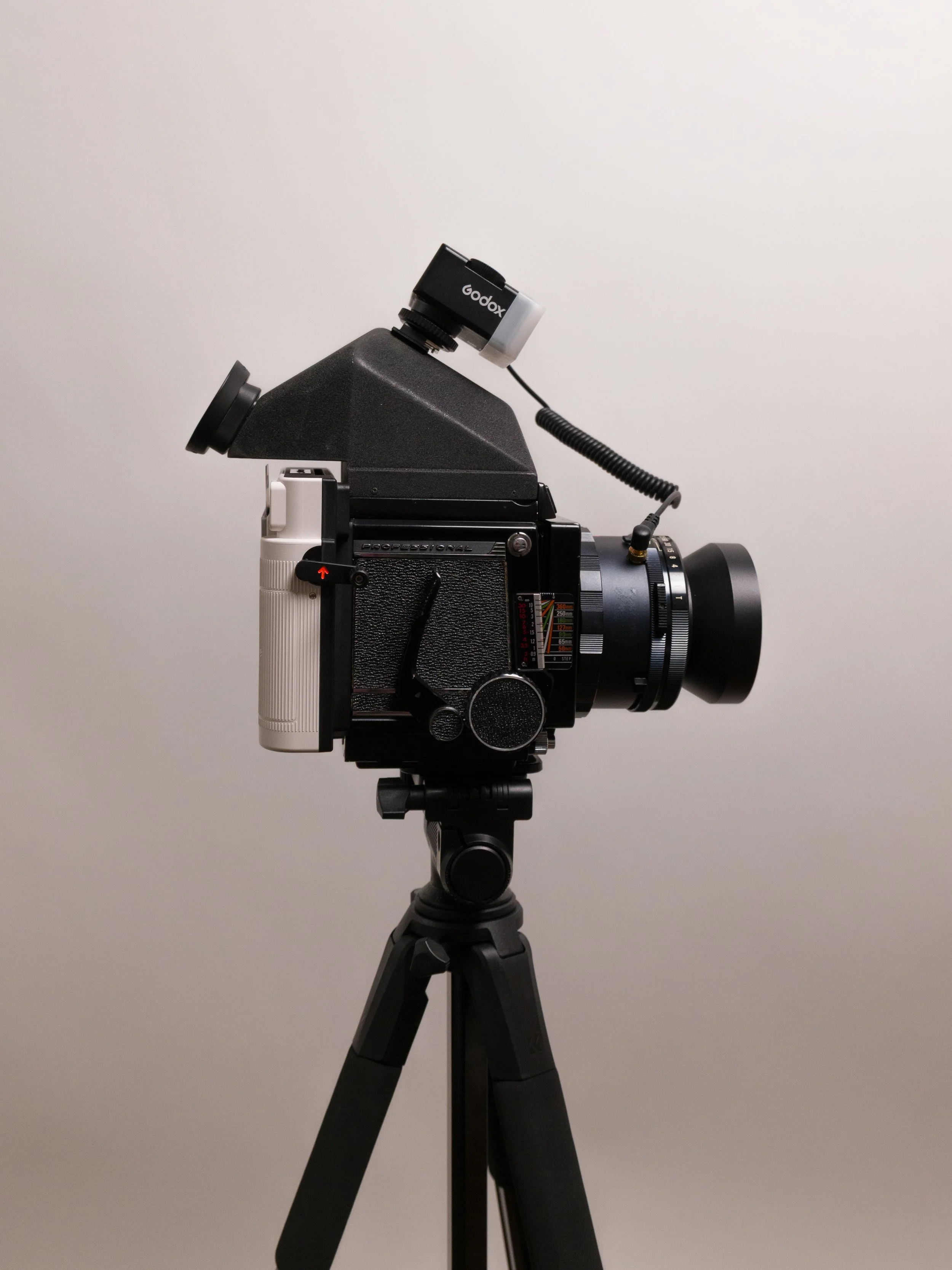 A vintage camera mounted on a tripod with a microscope attached to the top, set against a plain background.
