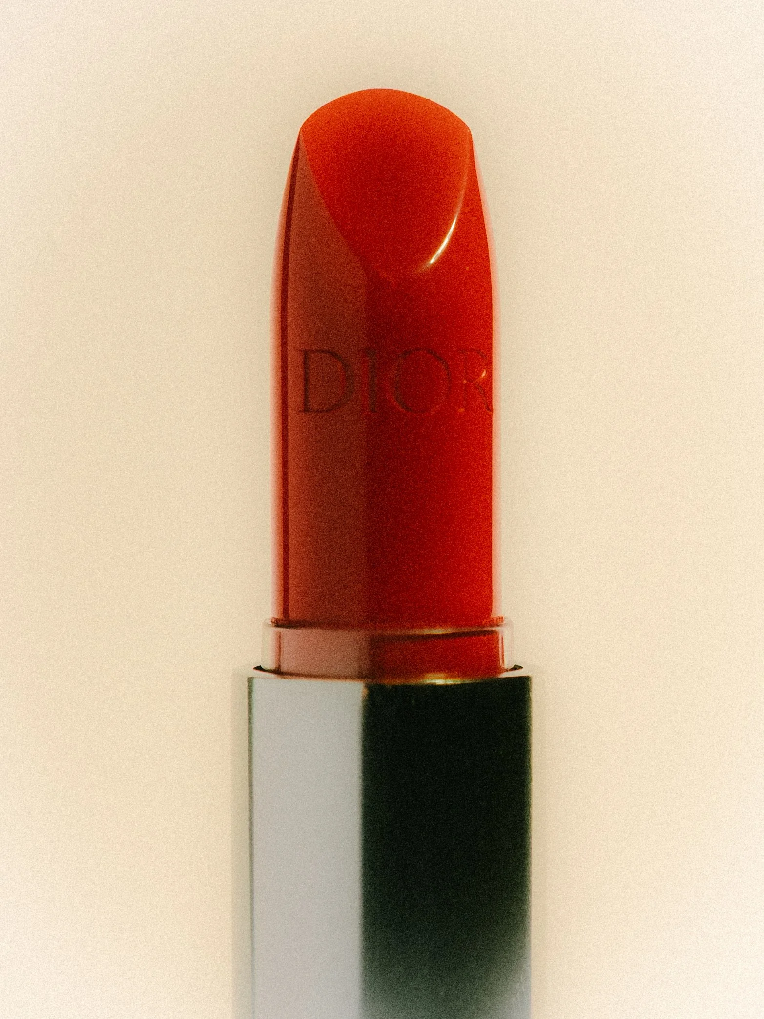 A red lipstick with a clear cap and a black base, standing upright against a light background.