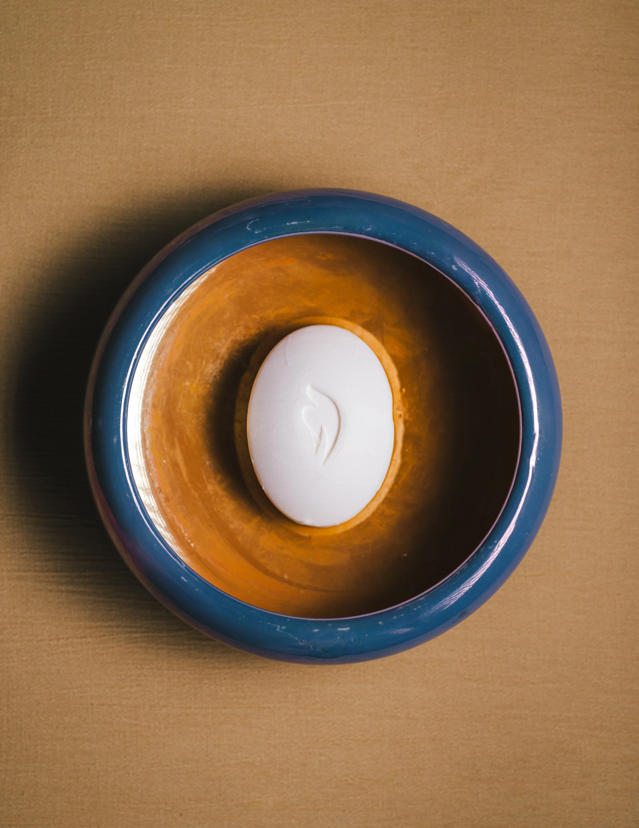 A round blue ceramic bowl with a white candle inside, placed on a wooden surface.