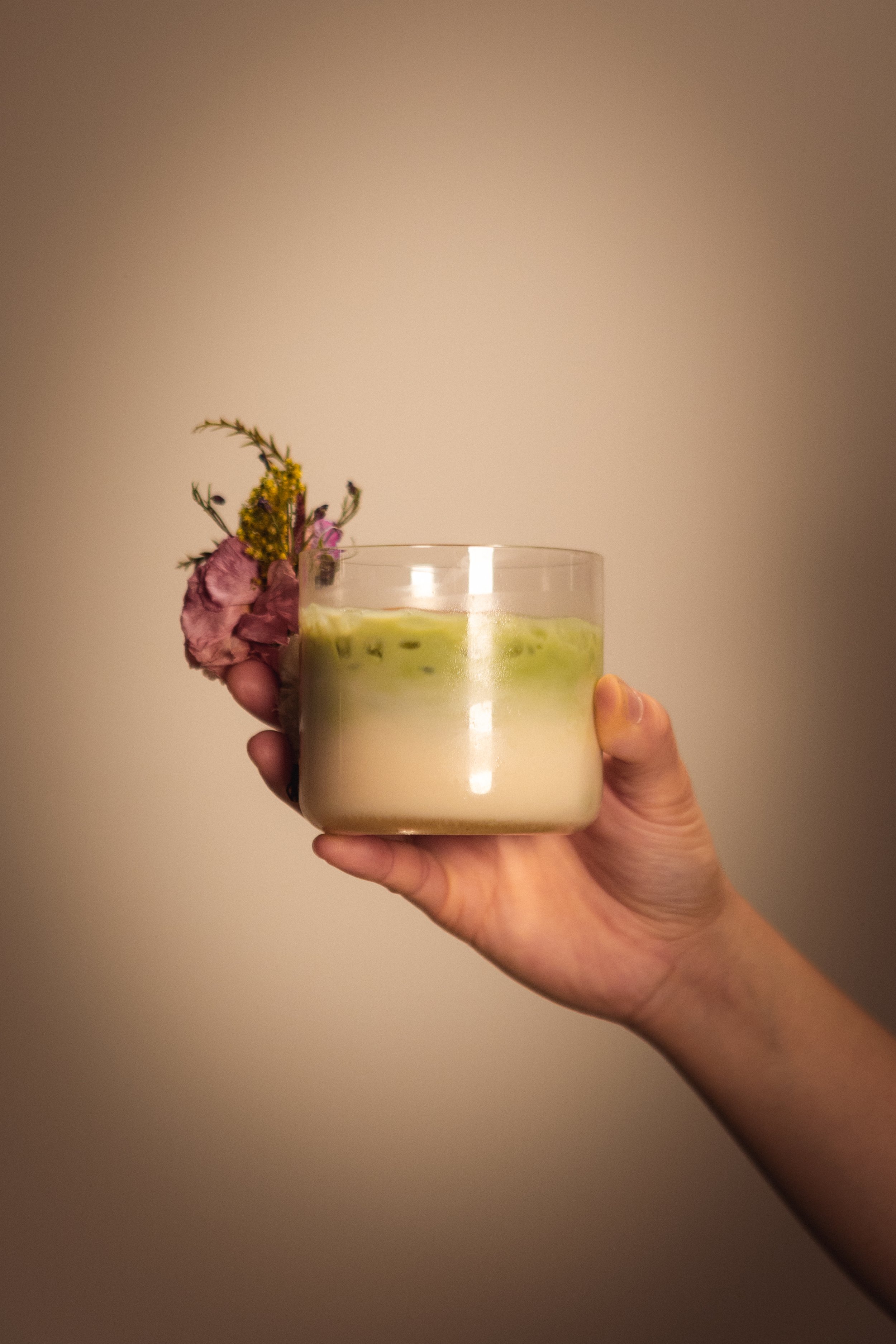 A hand holding a glass with a light green beverage, garnished with pink and yellow flowers. Columbus, Ohio, David Kim Photography