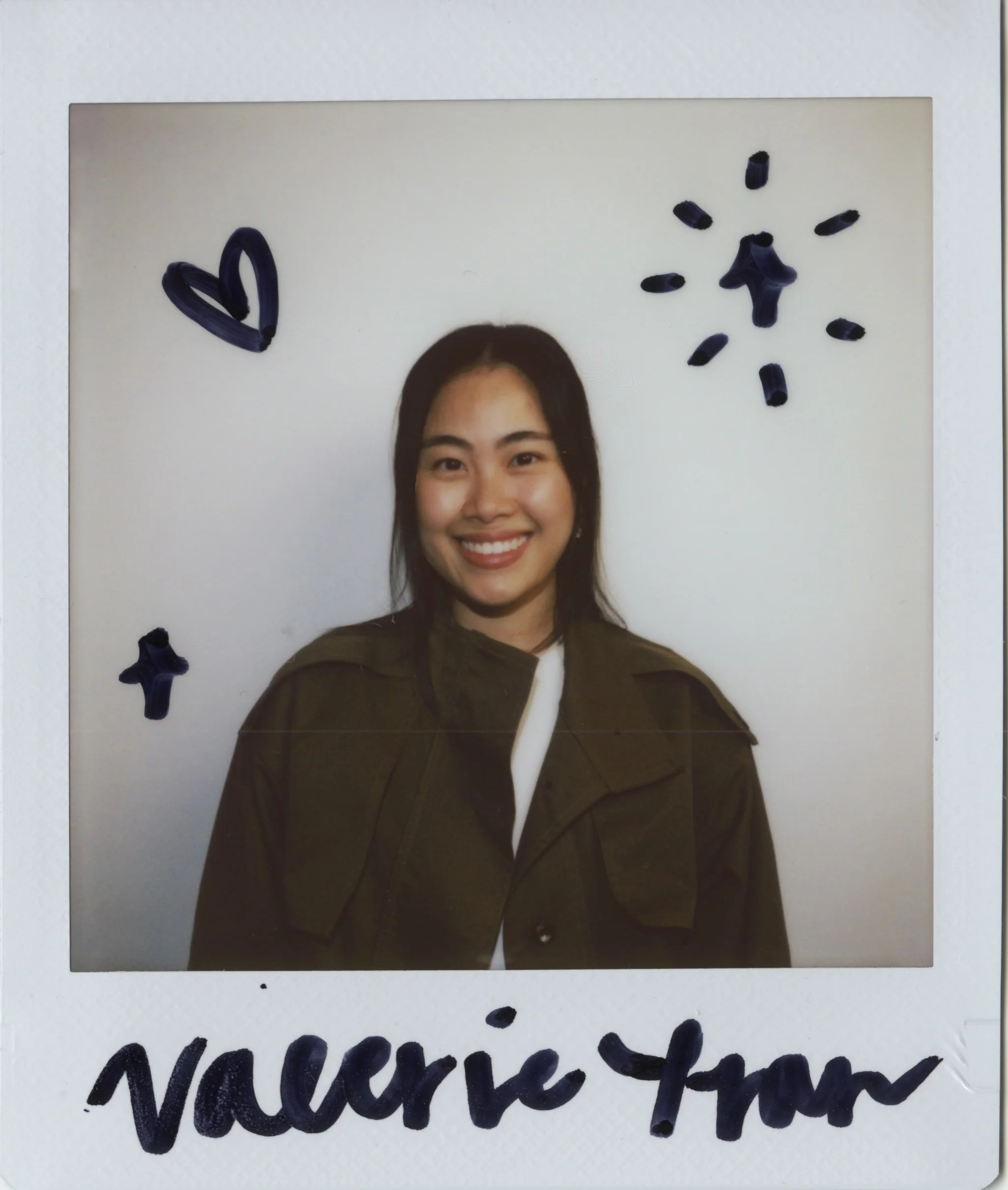 Physical polaroid photo of a woman with long dark hair smiling. The polaroid has hand-drawn blue hearts and lines, and handwritten text in black marker.