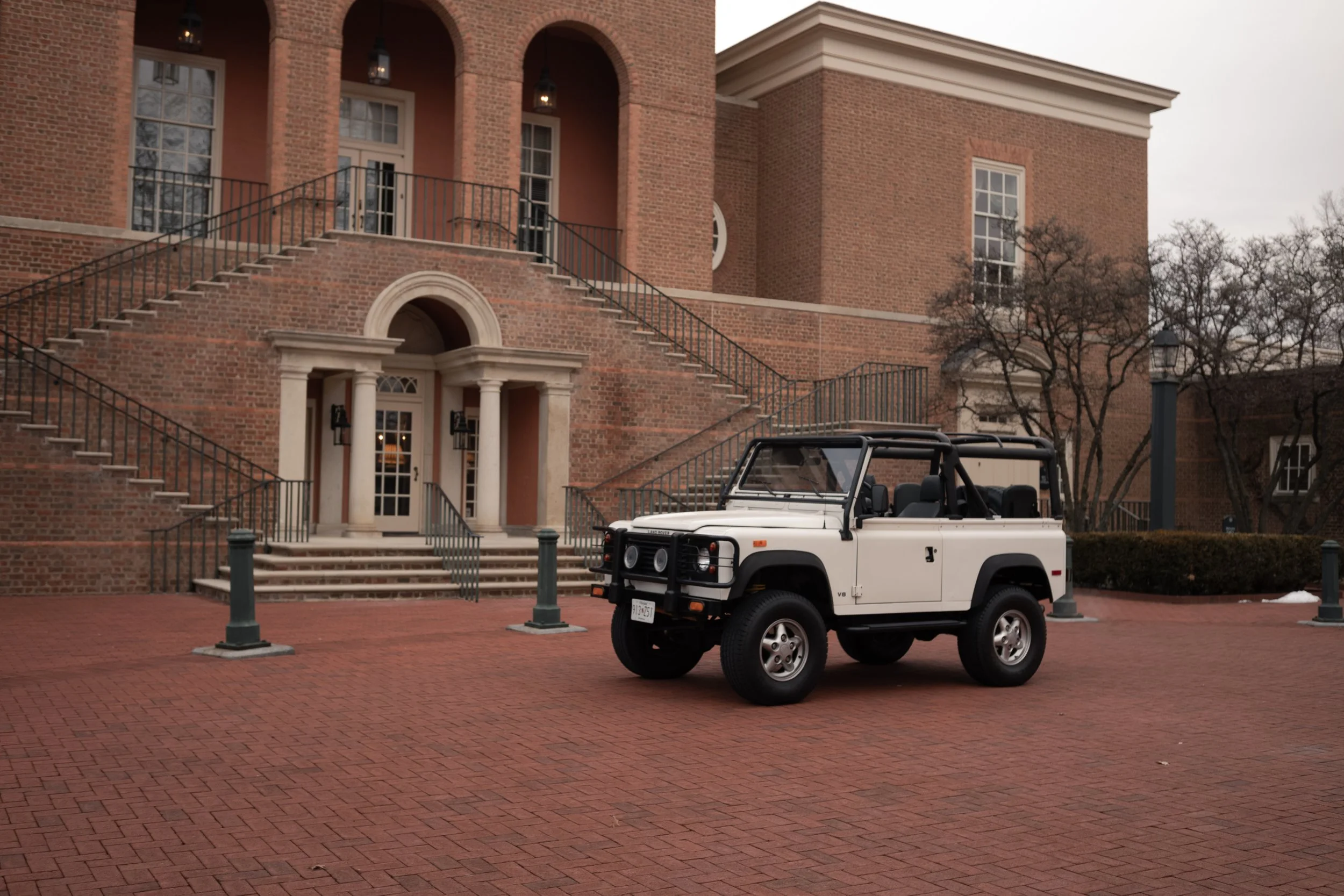 A white off-road vehicle parked in front of a large brick building with multiple staircases, windows, and trees without leaves. Columbus, Ohio, David Kim Photography