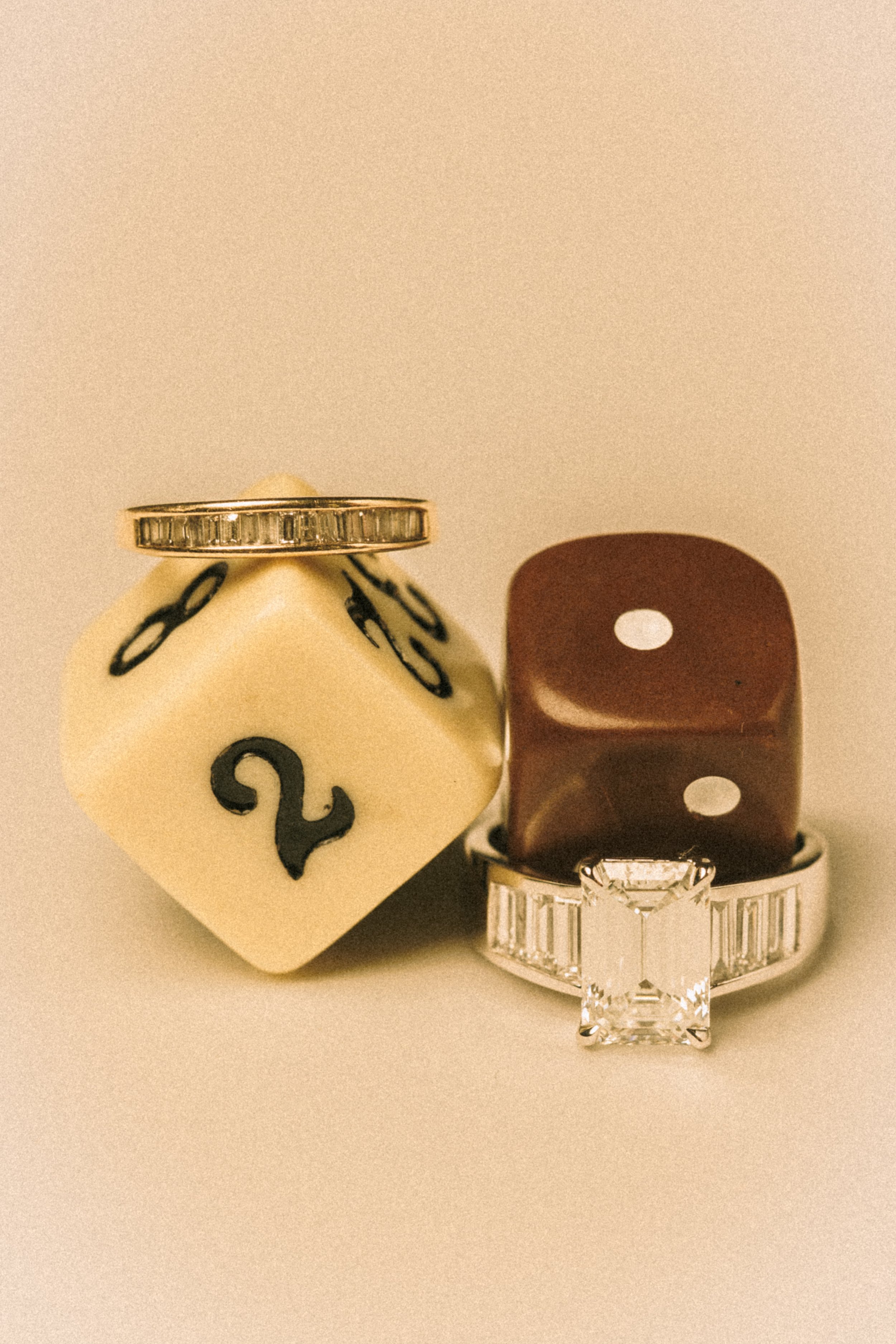 A gold ring with embedded diamonds displayed on a small, rounded white holder with black decorative markings, next to a brown chess piece and a large, clear, square-cut diamond—possibly a ring, jewelry, or jewelry display.