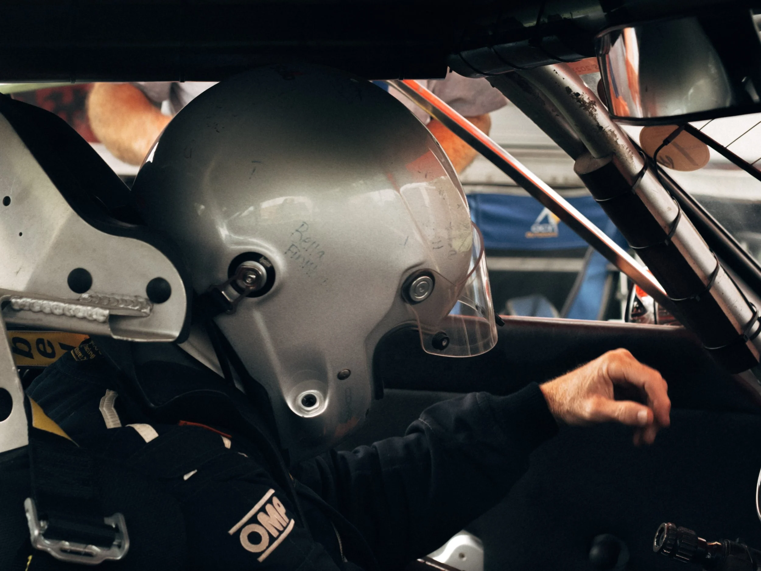 Close-up of a person wearing a gray helmet and racing suit, sitting on a motorcycle with visible suspension and brake components.