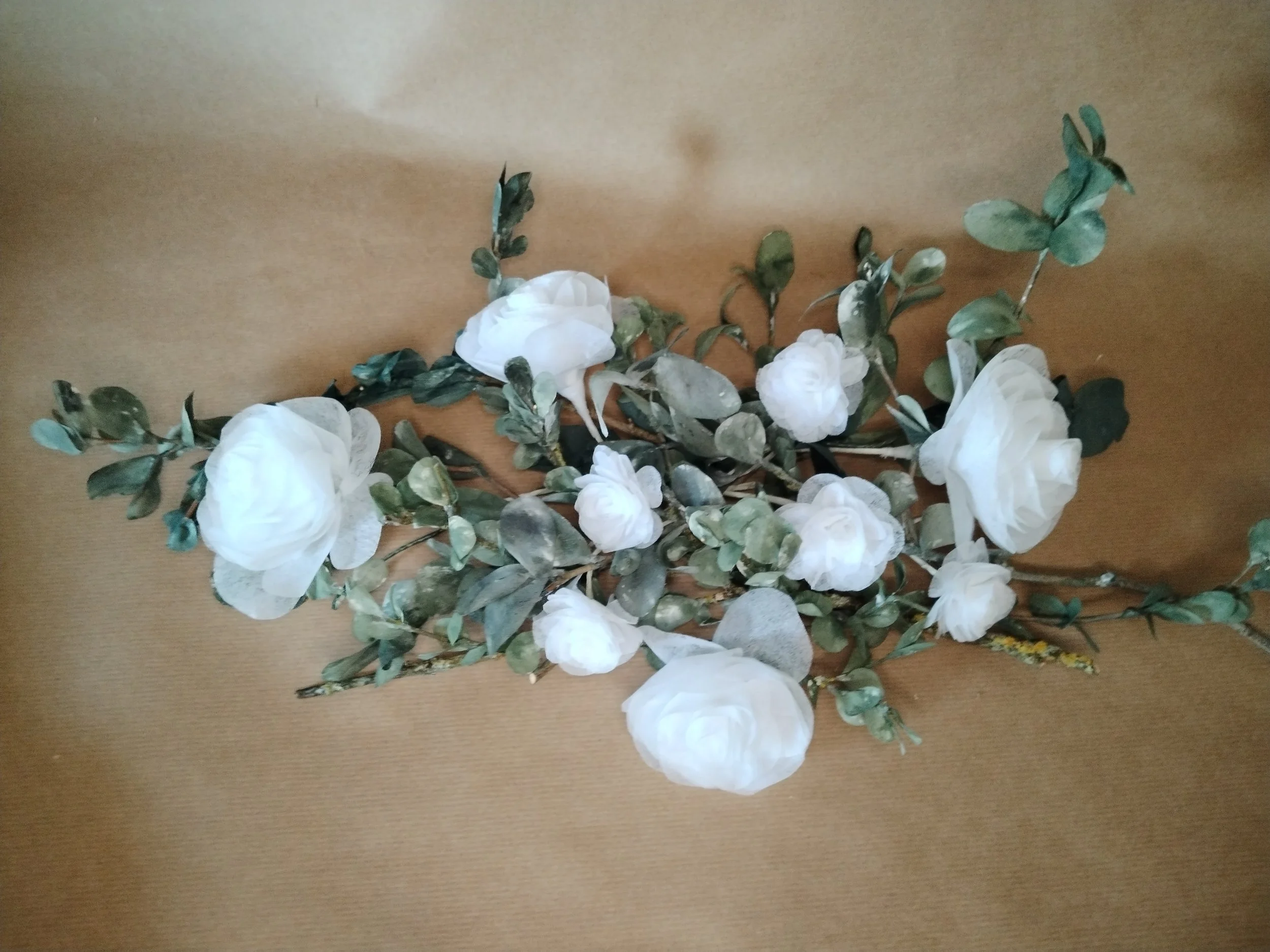 Un arrangement floral avec des roses blanches et des feuillages verts posé sur une surface en bois.