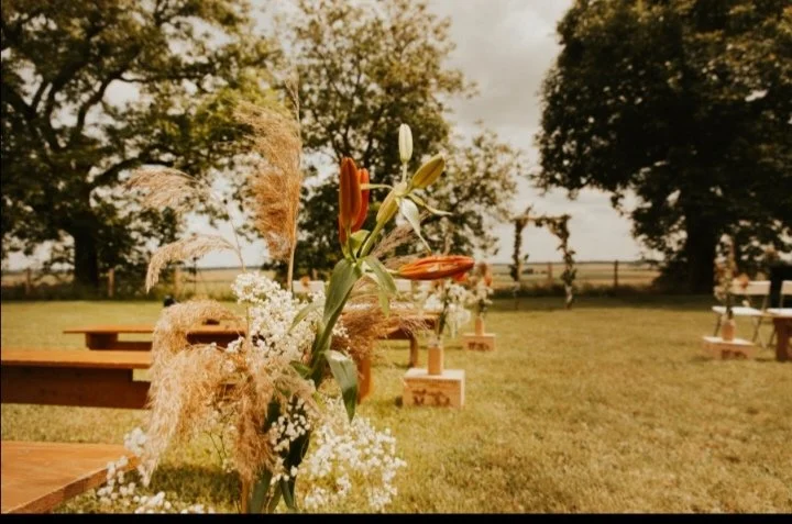 Vase de fleurs contenant un lys blanc, une rose orange, des fleurs de gypsophile et de la pampa, fleurs naturelles des champs, chic et champêtre, installé sur une table lors d'une cérémonie de mariage athée en plein air